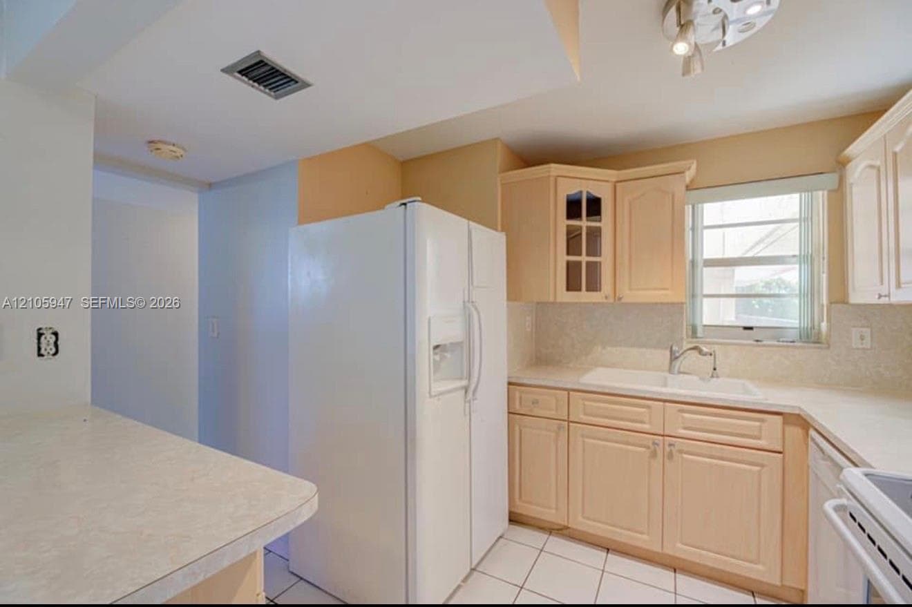 Kitchen featuring light-finish cabinetry, white countertops, tile flooring, built-in refrigerator, and sink with chrome-finish faucet