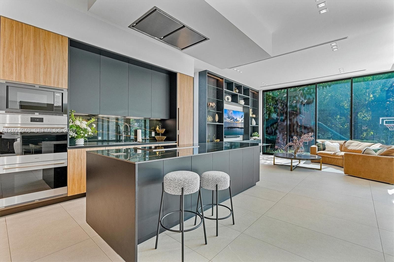 Contemporary kitchen featuring flat-panel cabinetry, a central island with a waterfall edge, stainless steel built-in double wall ovens, ceiling-integrated recessed lighting, and floor-to-ceiling glass wall panels