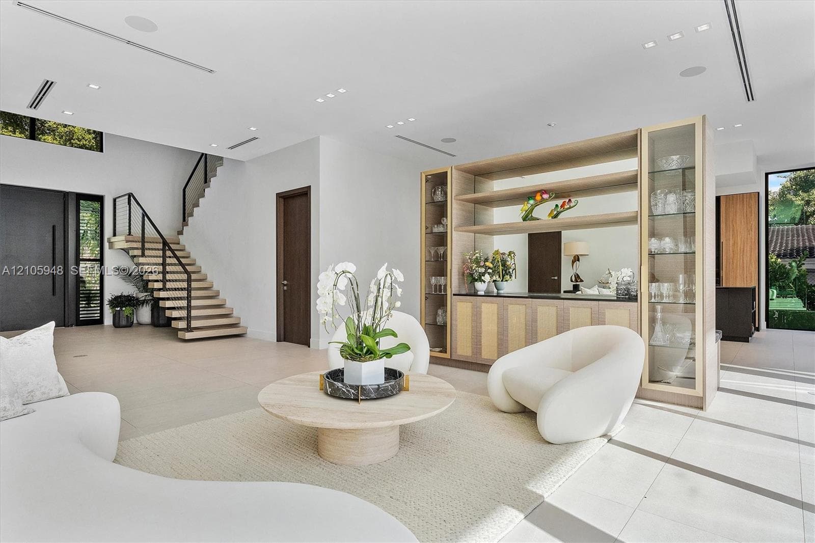 Open floor plan featuring a floating staircase with metal railings, built-in floor-to-ceiling cabinetry with glass display shelving, recessed ceiling lighting, and large-format tile flooring