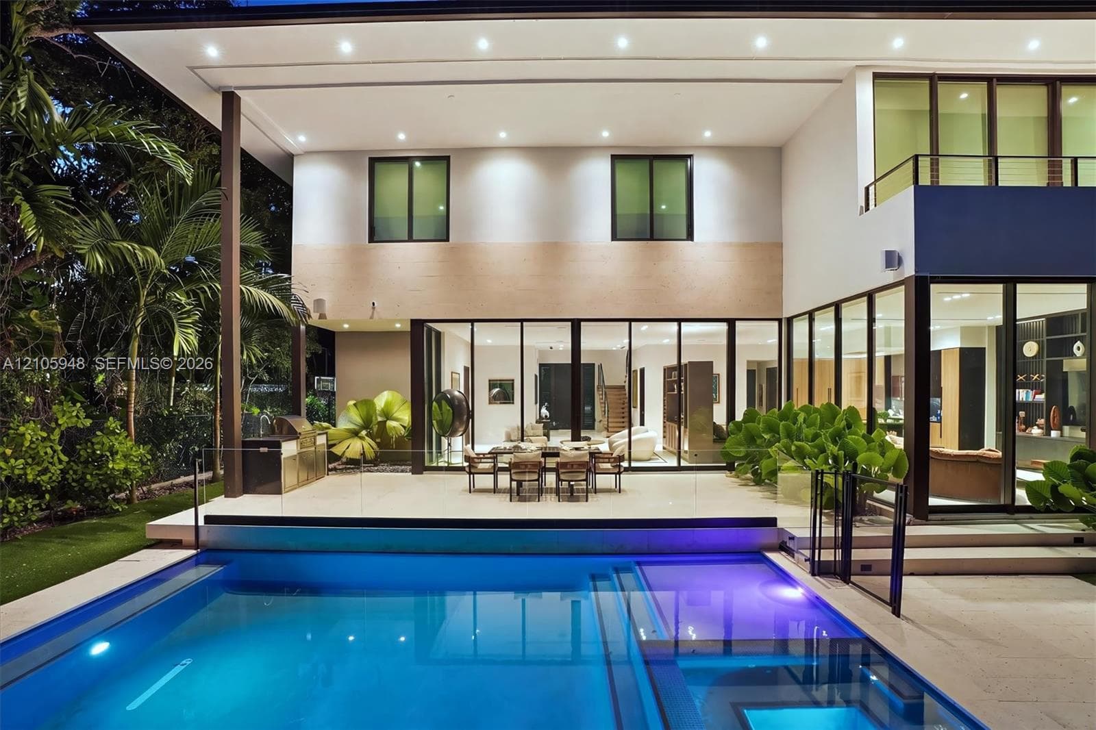Contemporary two-story residence featuring expansive floor-to-ceiling glass wall panels, an integrated outdoor kitchen, a built-in swimming pool with a sun shelf, and a covered paved patio