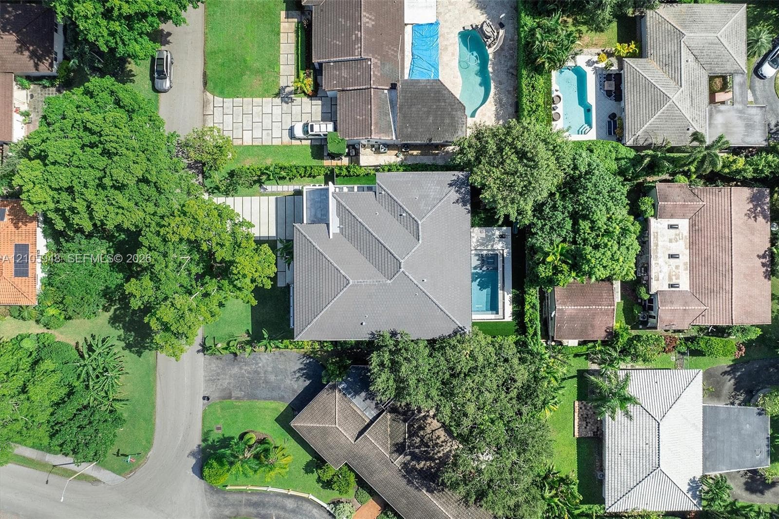 Aerial perspective featuring a hip-roof structure, rectangular swimming pool, paved driveway, and mature landscaping