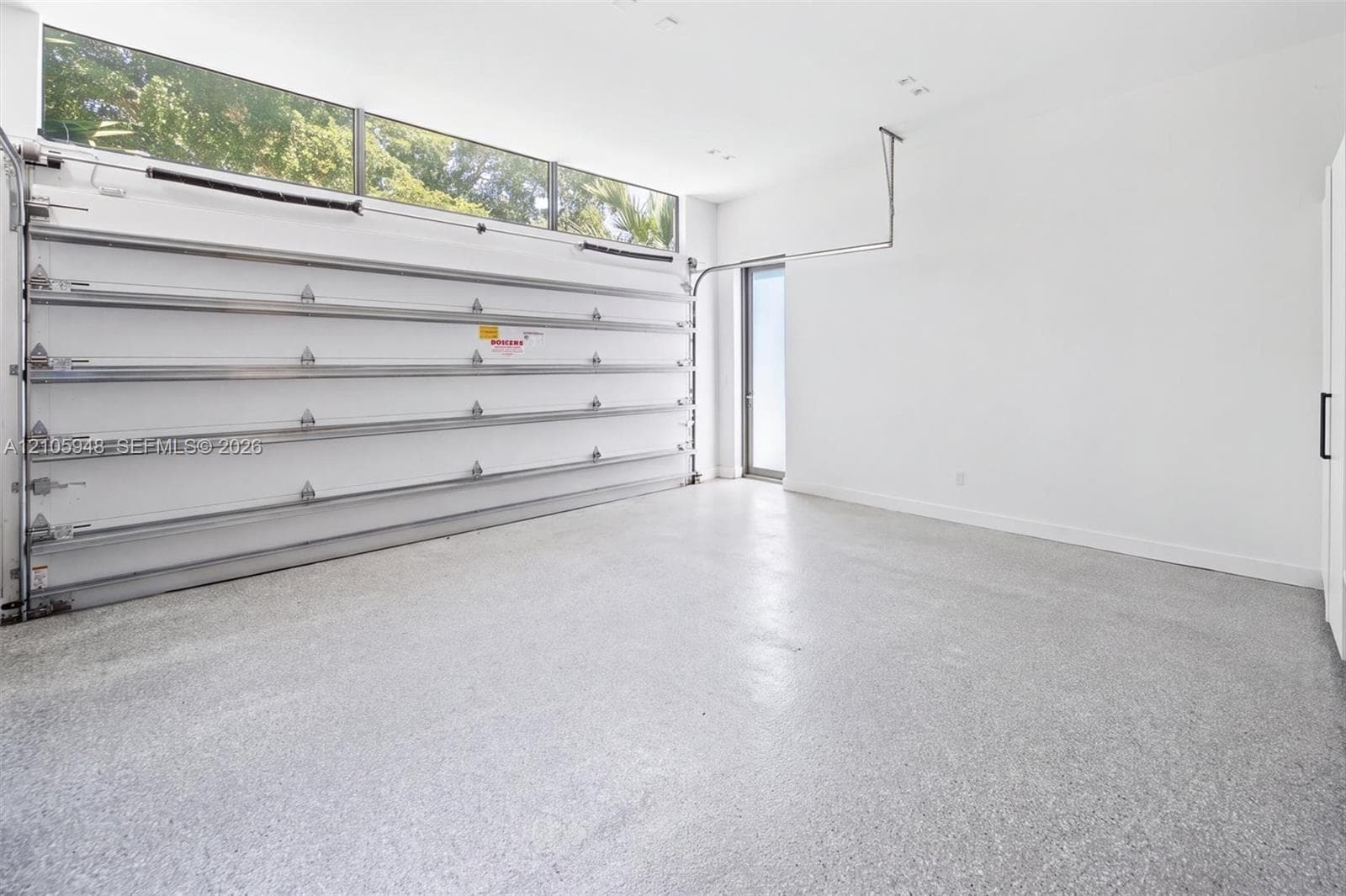 Garage space featuring speckled epoxy flooring, white paneled walls, a ceiling-mounted automatic door opener, and a row of horizontal transom windows