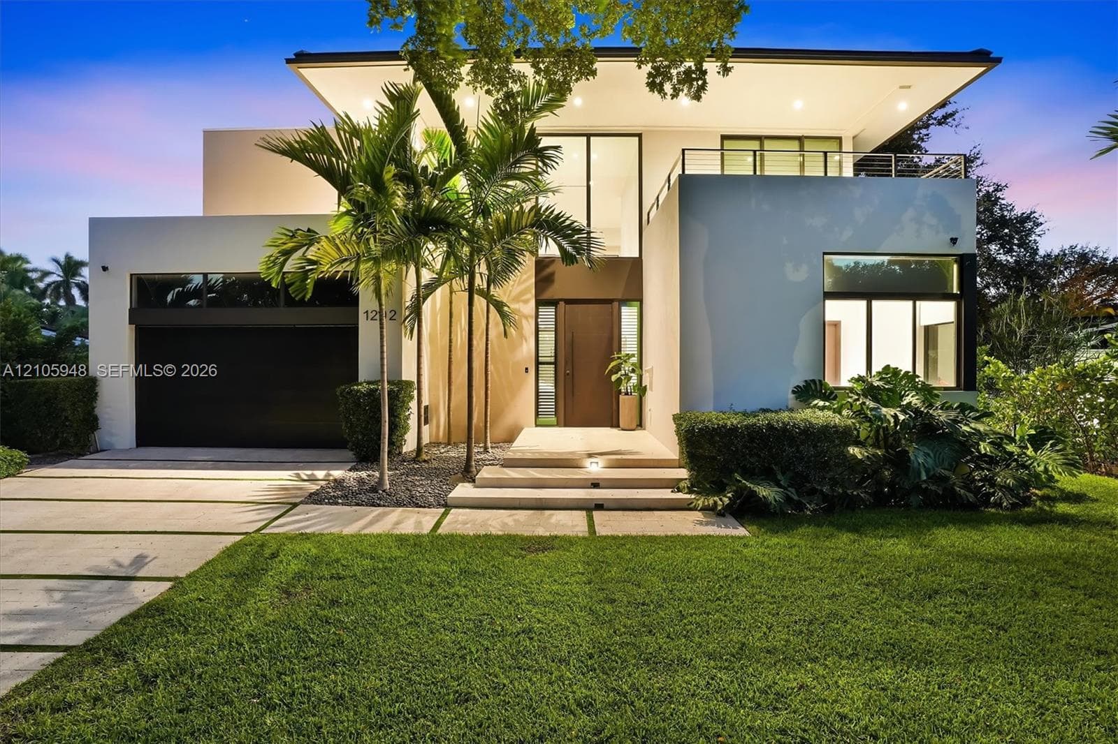 Contemporary architectural exterior featuring a stucco facade, second-story balcony with metal railing, oversized glass entryway, and a concrete paver driveway