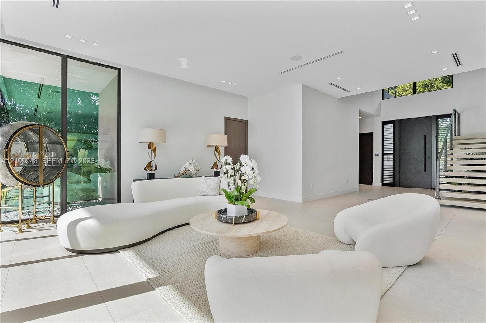 Open-concept living space featuring large-format tile flooring, floor-to-ceiling glass panel walls, recessed ceiling lighting, and a staircase with open risers