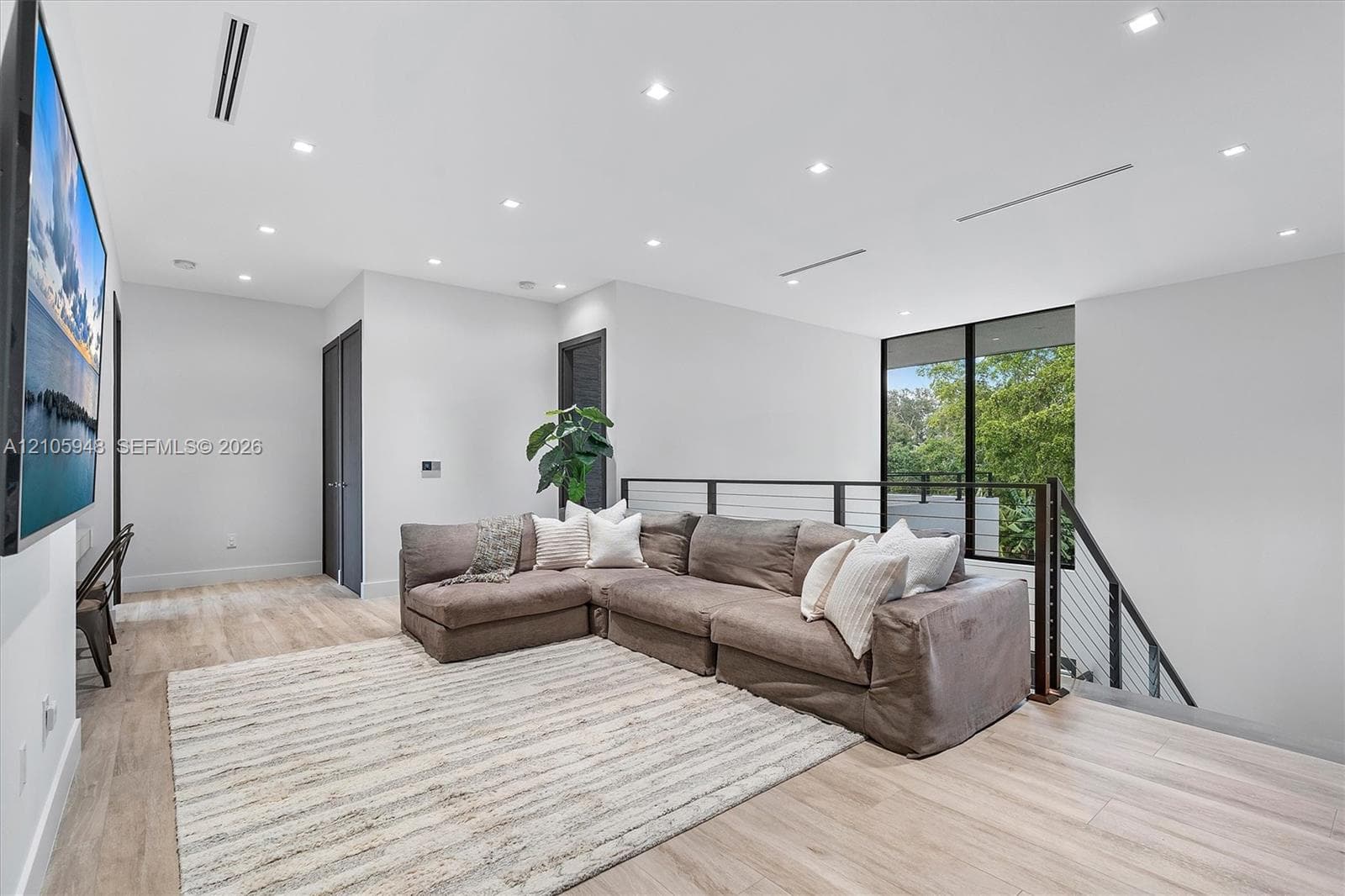 Open-concept space featuring light wood-finish flooring, recessed ceiling lighting, linear HVAC diffusers, and a staircase with a horizontal cable railing system