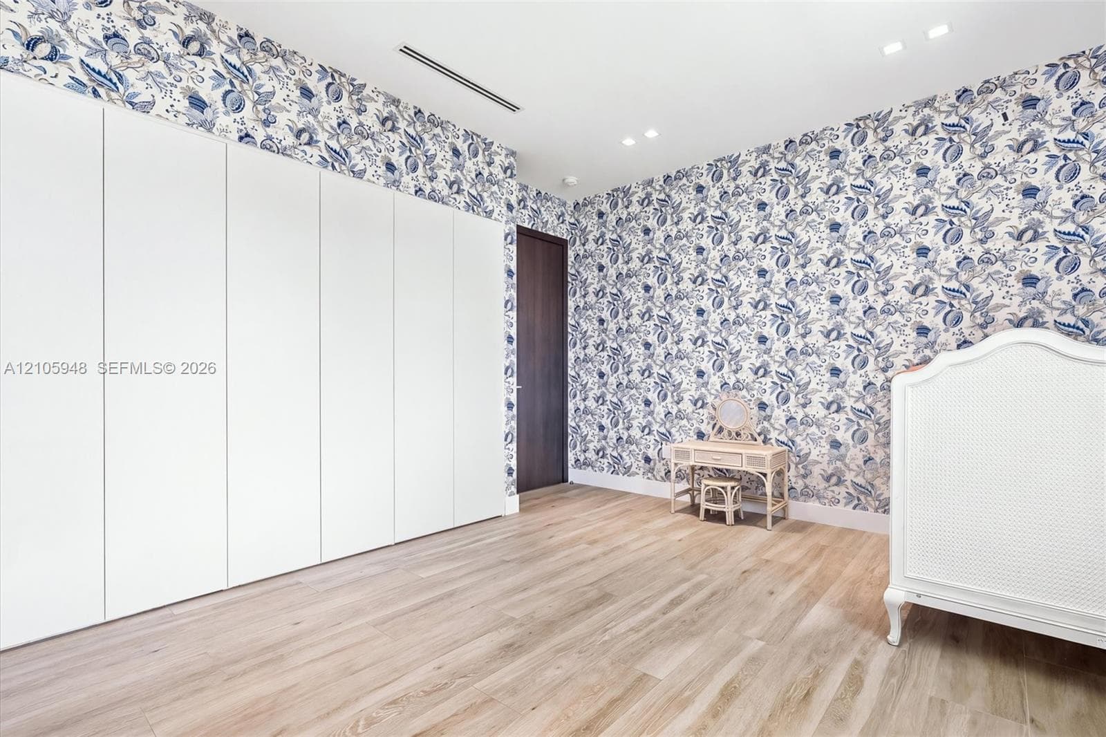 Room featuring floor-to-ceiling white cabinetry, wood-finish flooring, patterned wallpaper, recessed lighting, and a dark-finish door