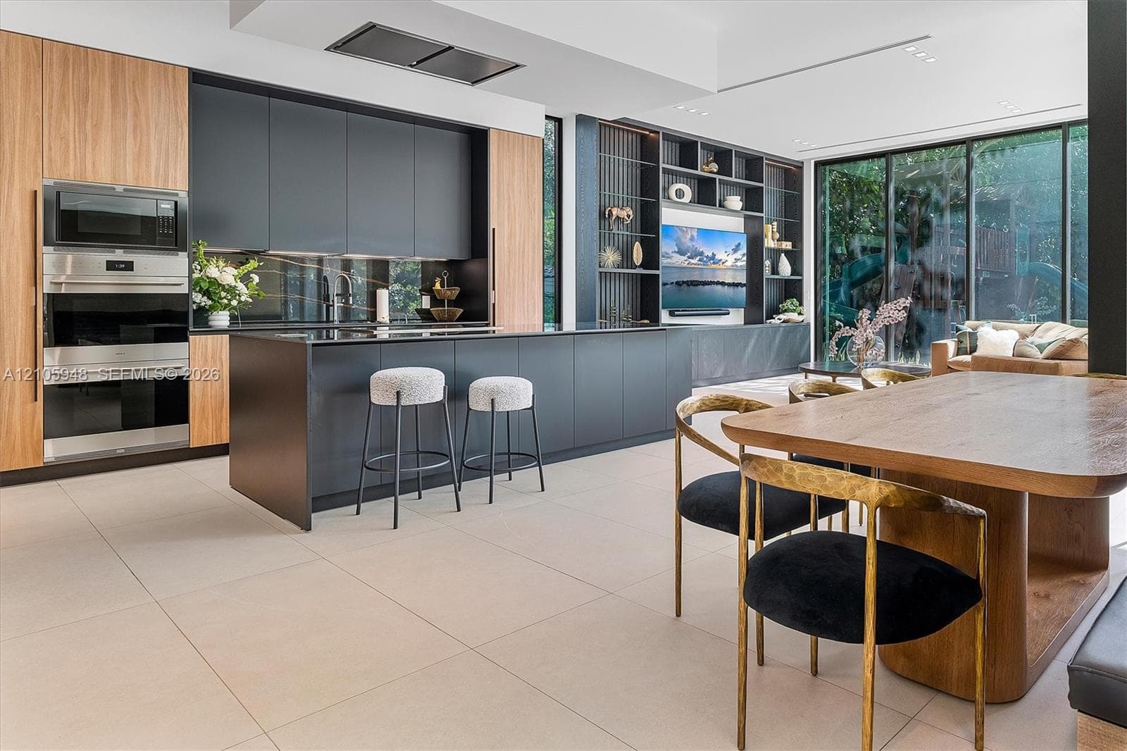 Contemporary kitchen featuring matte dark cabinetry, wood-finish cabinetry accents, a large center island, floor-to-ceiling glass walls, and integrated full-height shelving