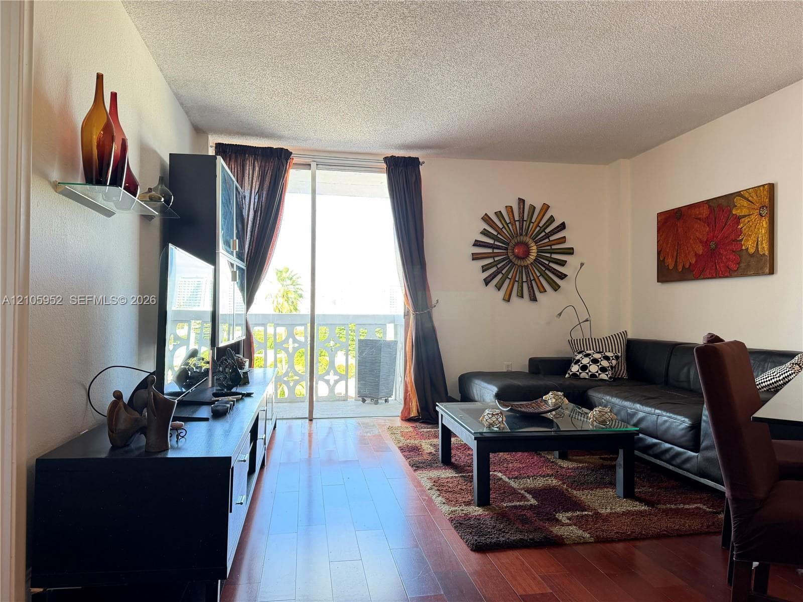 Living area featuring wood-finish flooring and floor-to-ceiling glass sliding doors providing access to a private balcony with decorative concrete railing