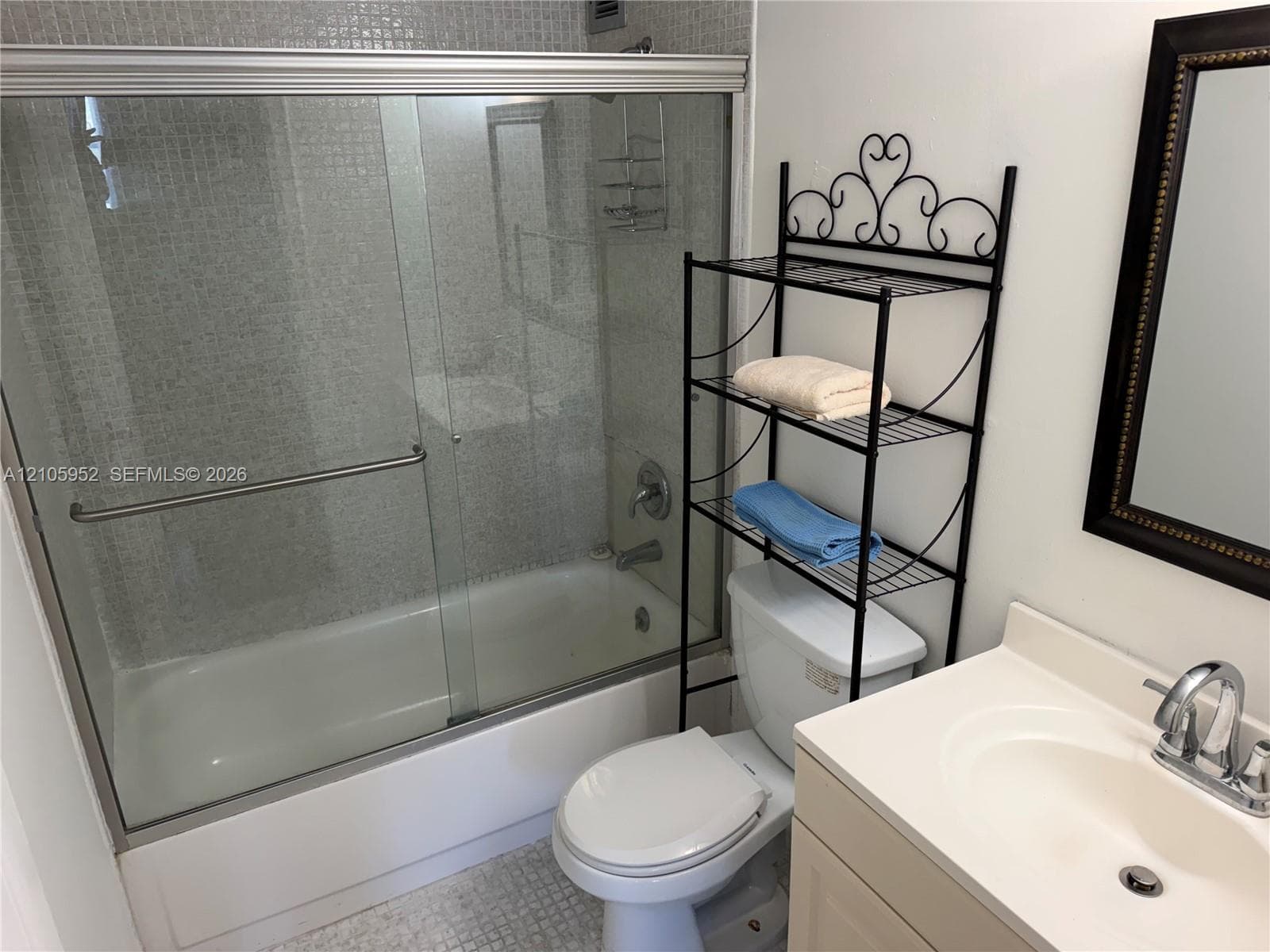 Bathroom featuring a shower-tub combination with a glass sliding enclosure, mosaic tile surround, vanity with an integrated basin, and chrome fixtures