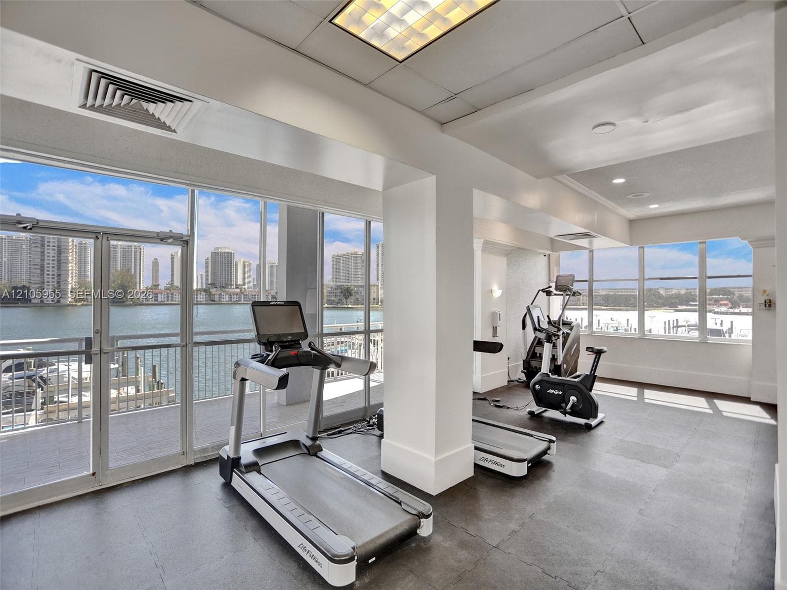 Fitness center featuring floor-to-ceiling windows, rubberized flooring, recessed lighting, and water frontage