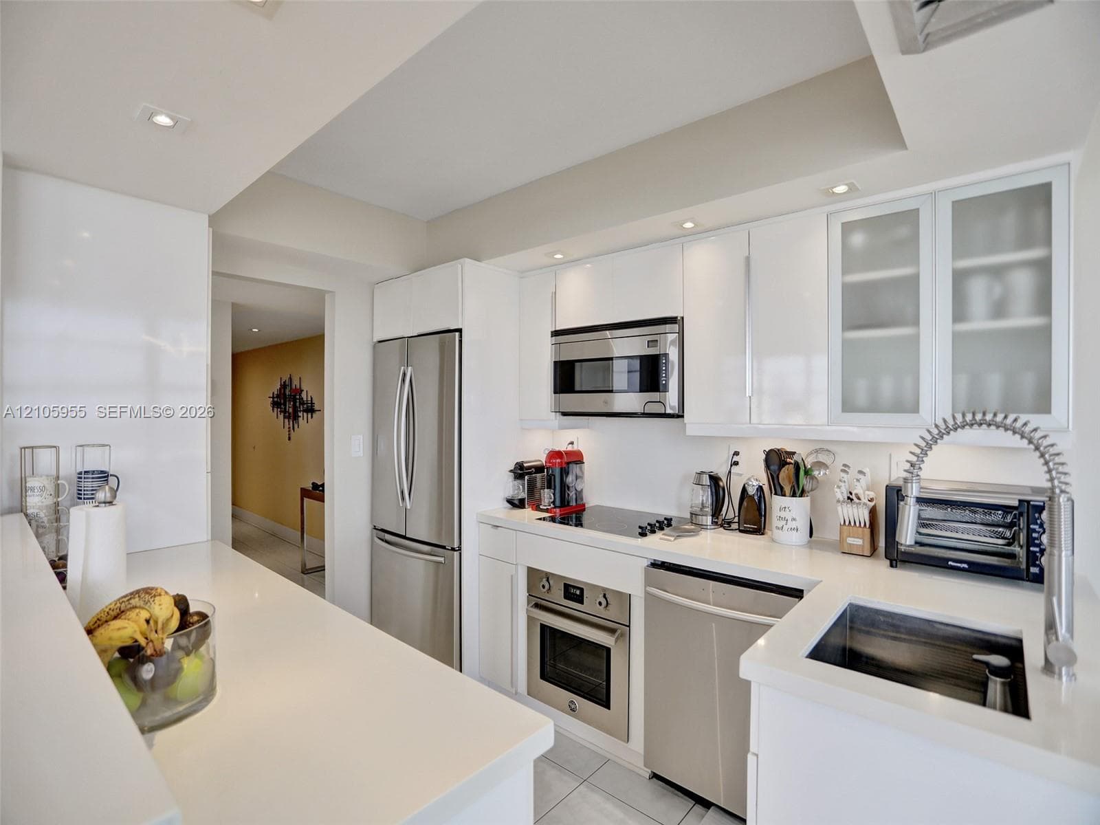 Modern kitchen featuring high-gloss white cabinetry, polished white countertops, stainless steel appliances, recessed ceiling lighting, and a gooseneck faucet