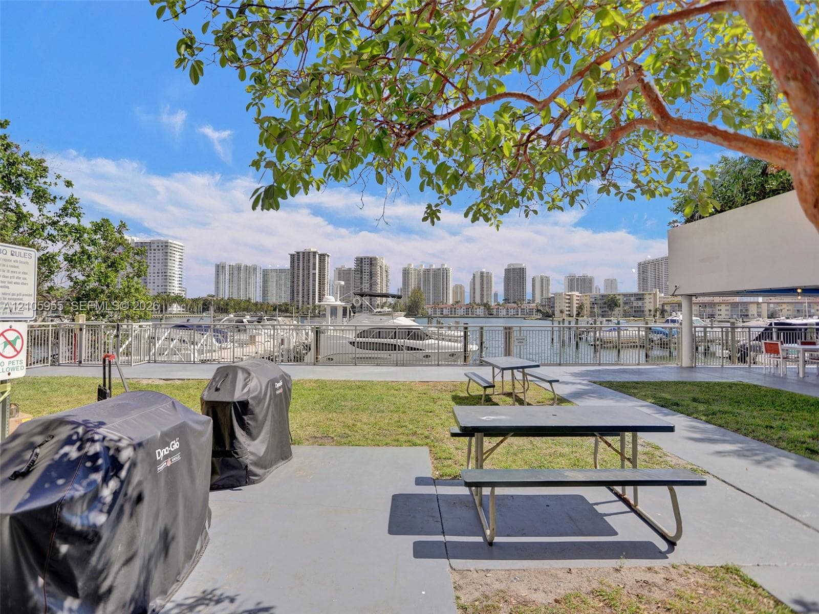 Waterfront grounds featuring a concrete patio, grassy lawn, metal perimeter fencing, and access to boat slips