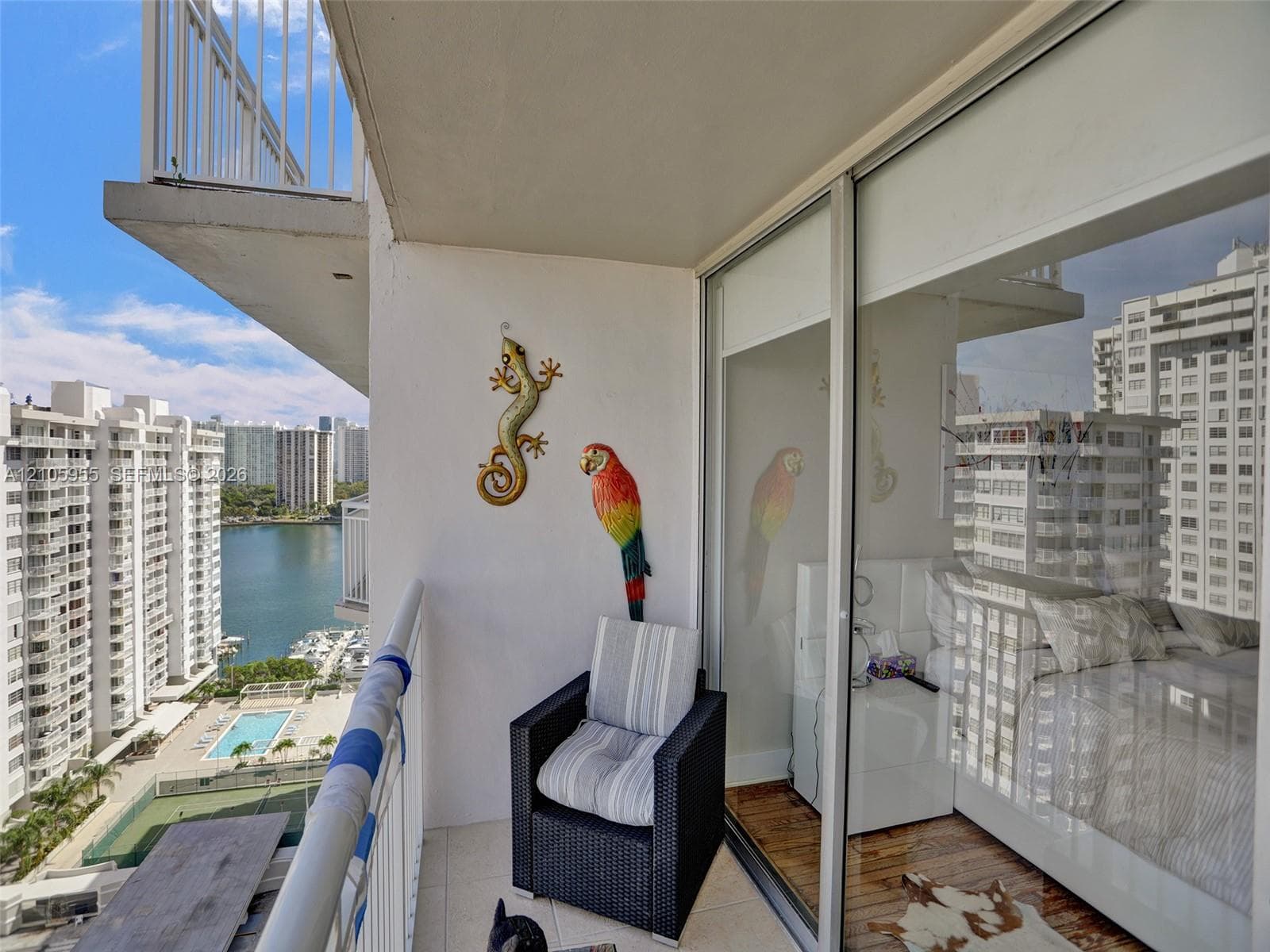 Covered balcony featuring white tiled flooring and a metal railing, floor-to-ceiling sliding glass doors, and panoramic urban and water surroundings