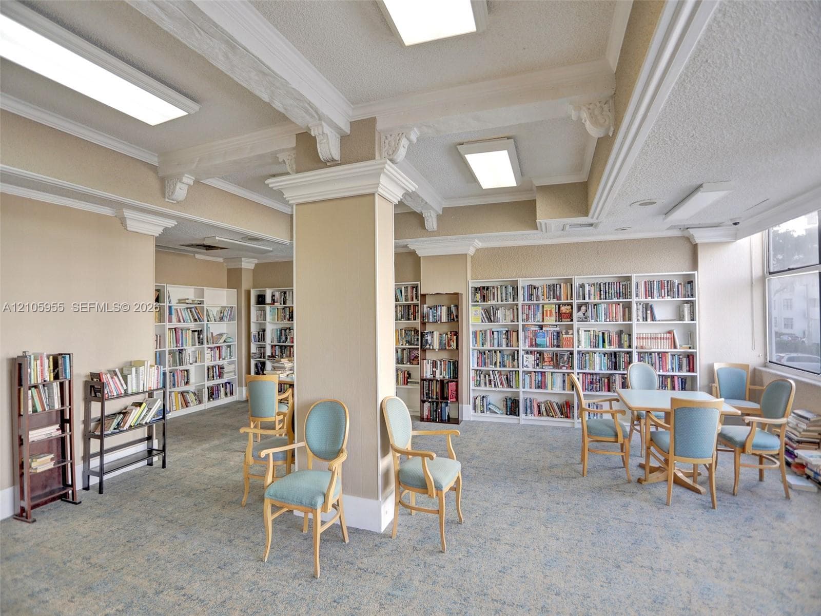 Built-in floor-to-ceiling shelving, decorative ceiling beams with crown molding, and large window placement providing natural light