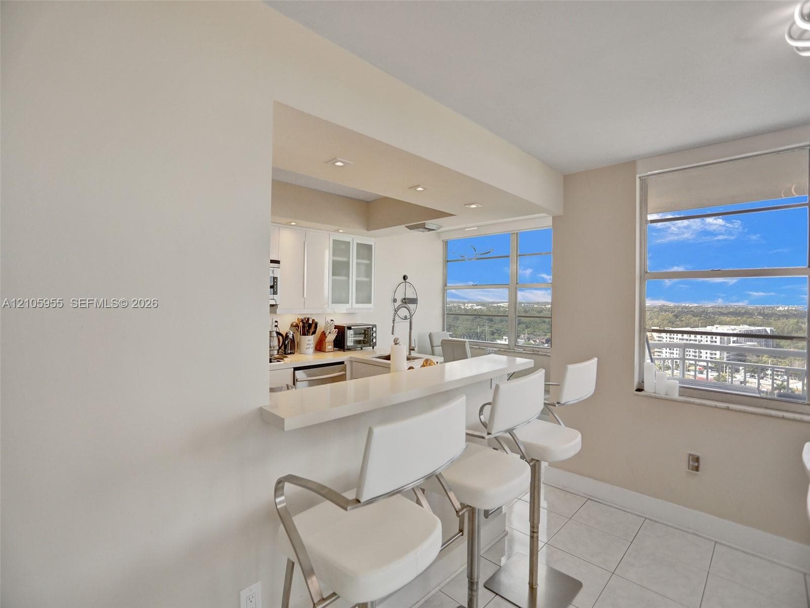 Kitchen featuring a white quartz breakfast bar, white cabinetry with glass-front accents, recessed lighting, and large windows with exterior scenery