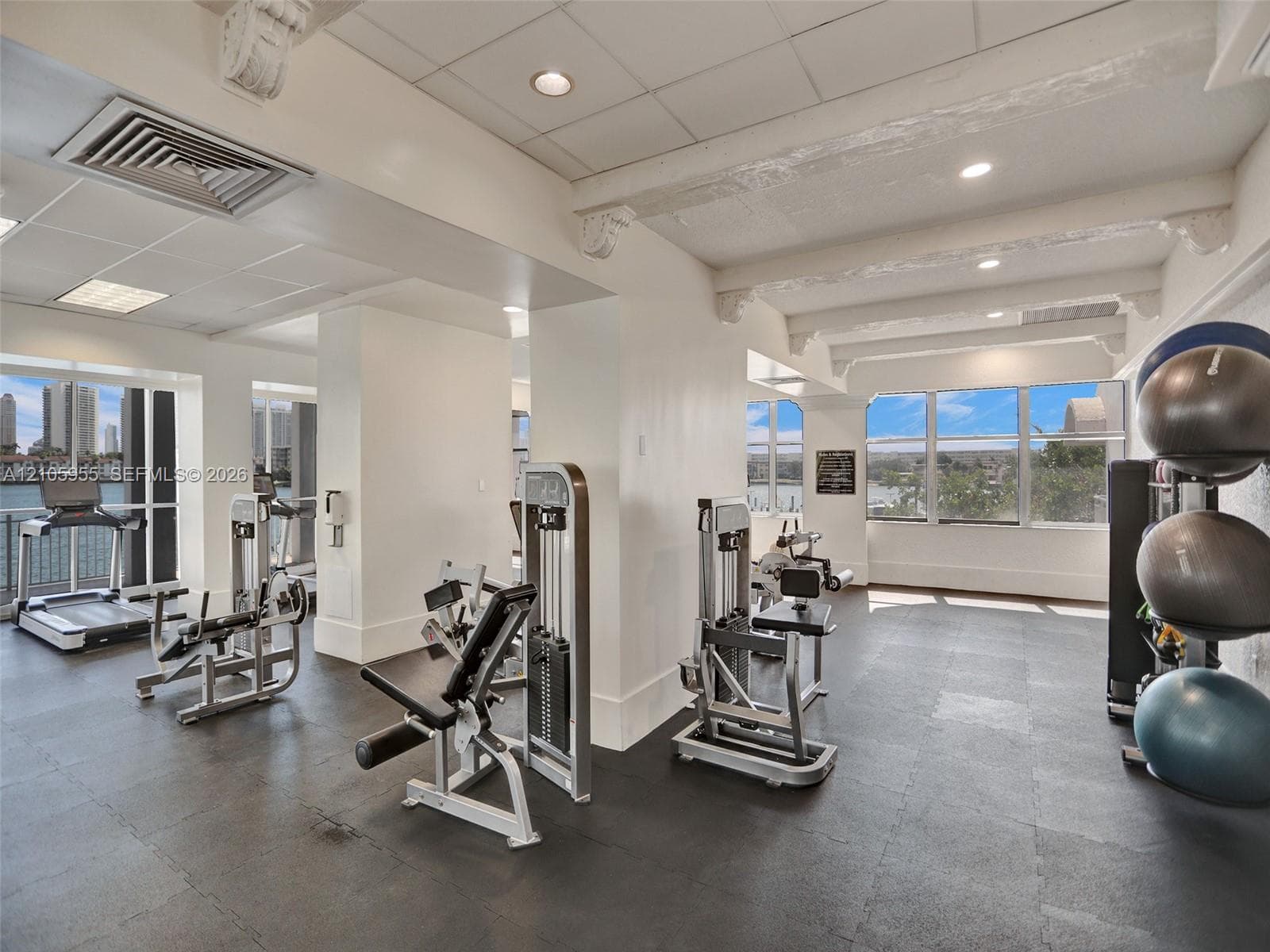 Fitness center featuring high ceilings with exposed decorative corbels, resilient flooring, extensive window walls, and recessed lighting