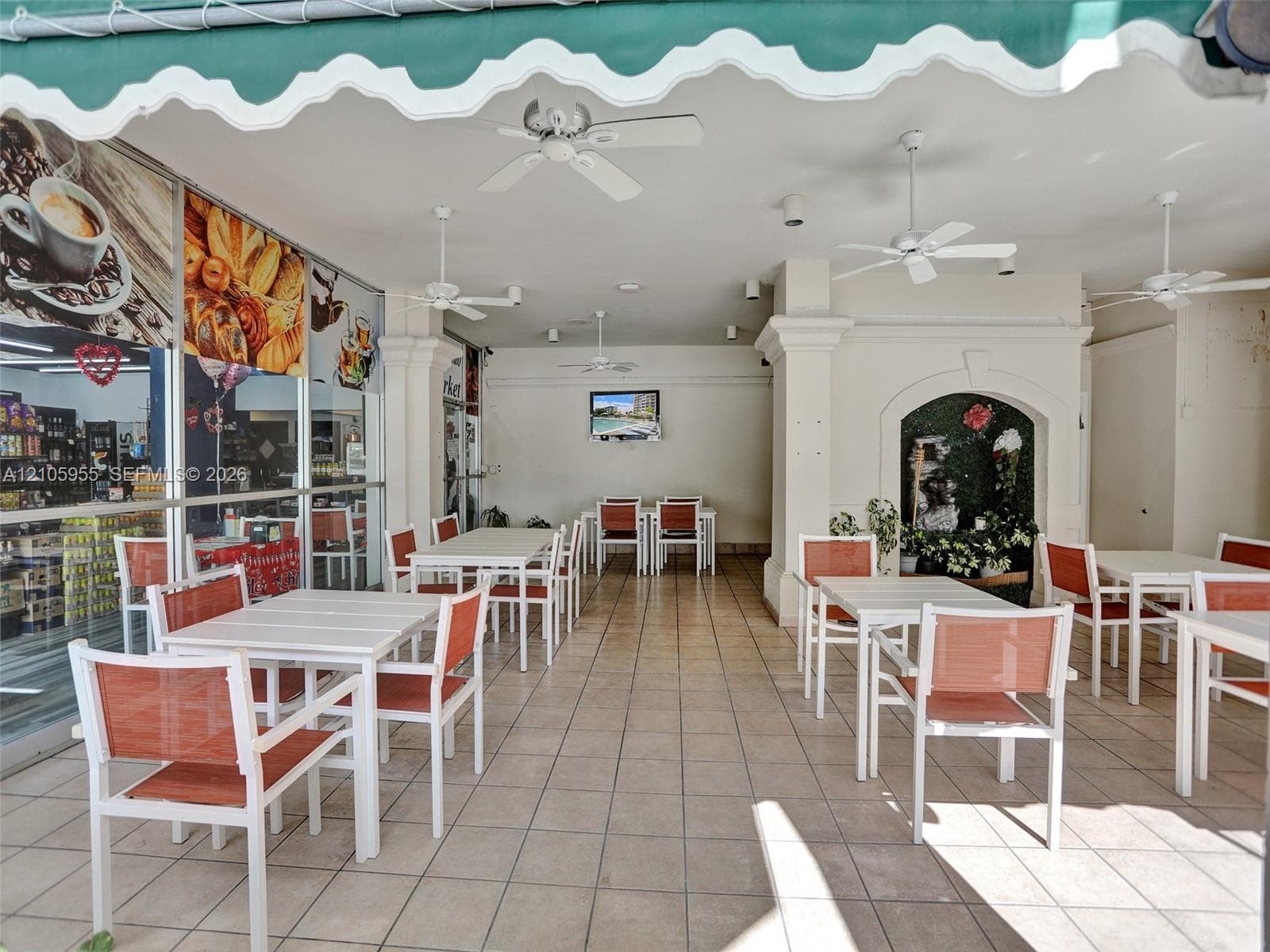 Covered outdoor patio featuring tile flooring, four ceiling fans, a scalloped fabric awning, and a decorative arched alcove