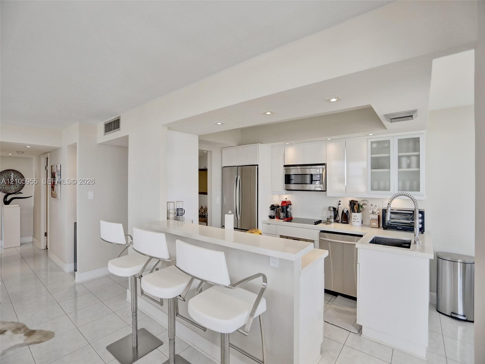 Kitchen featuring white cabinetry, quartz countertops, a peninsula with bar seating, stainless steel appliances, and tile flooring