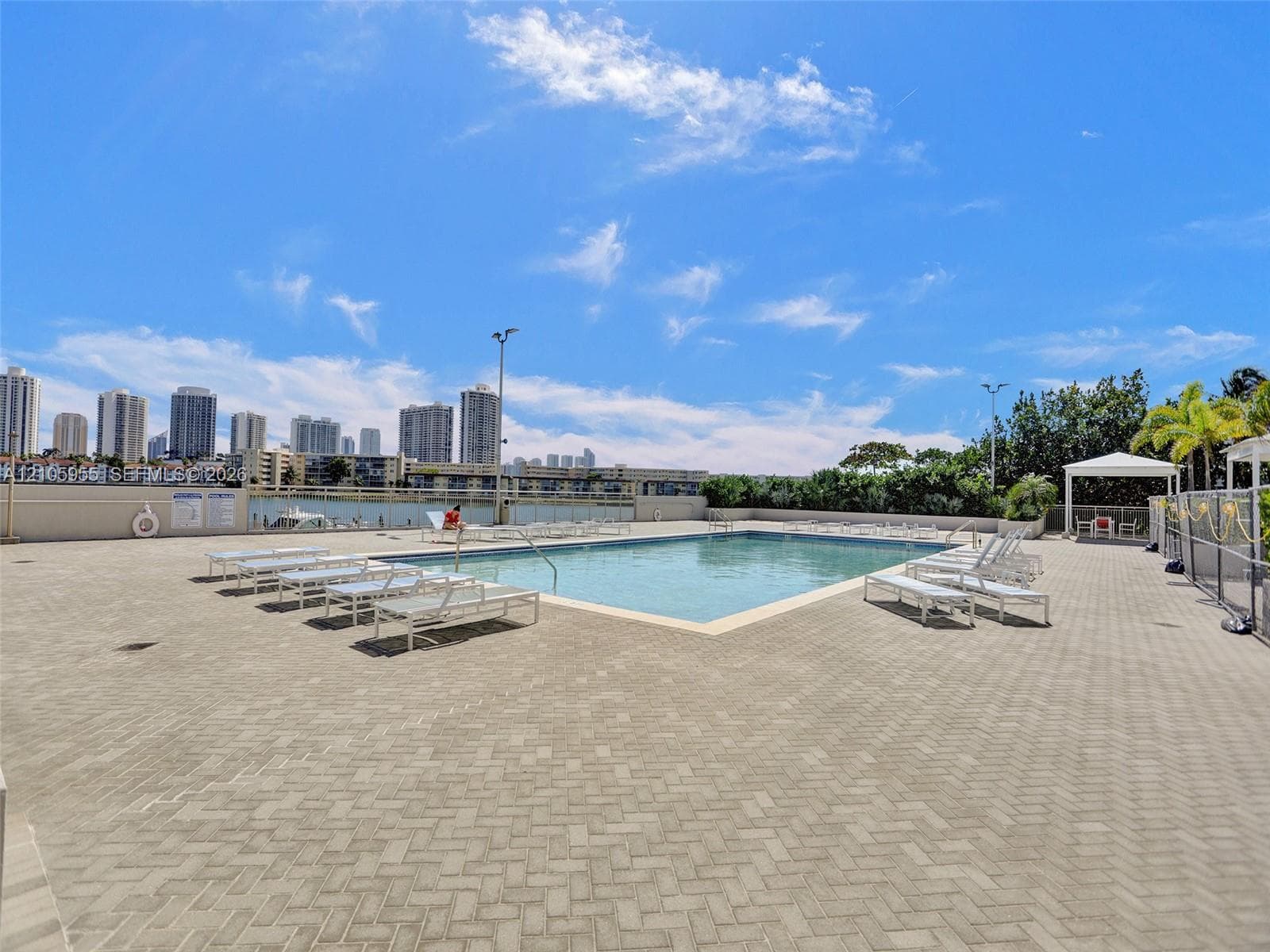 Swimming pool with a paved deck, perimeter fencing, and an overhead pavilion structure