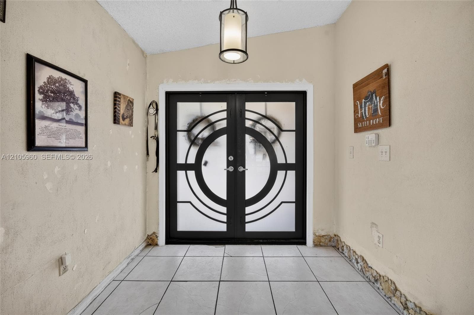 Entryway featuring double doors with geometric patterned glass inserts, tile flooring, and a central pendant light fixture