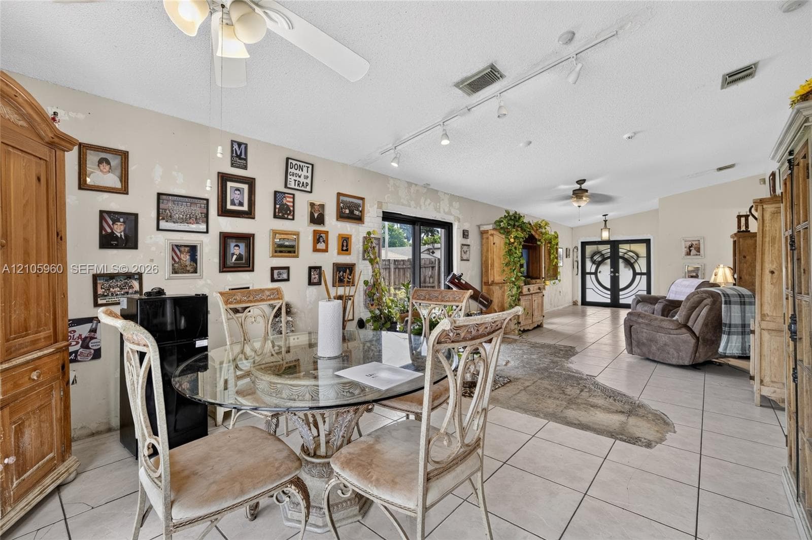 Open-concept interior featuring light-toned floor tiling, track lighting, ceiling fan fixtures, and double-entry glass-paneled doors