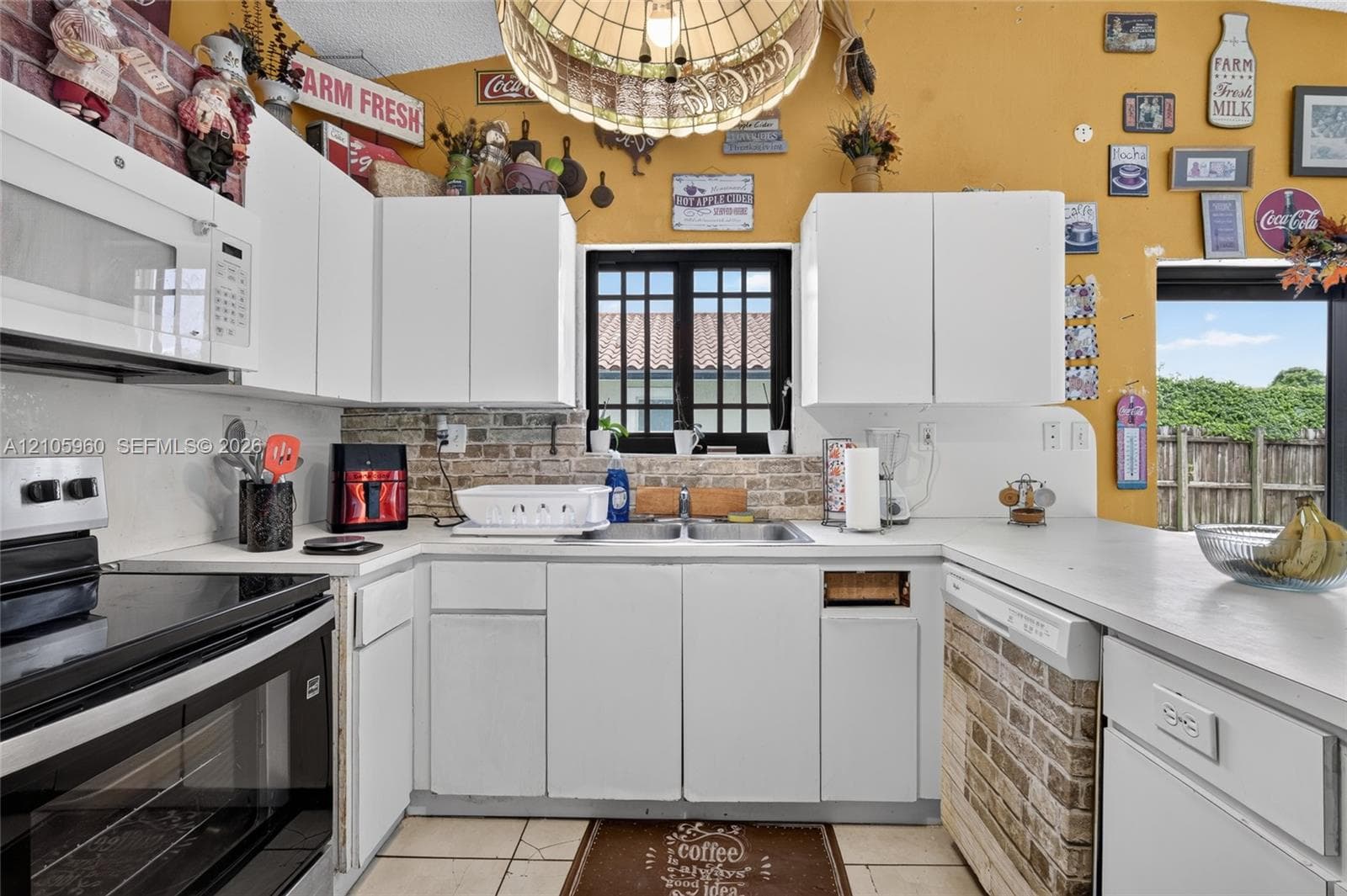 Kitchen featuring white cabinetry, brick backsplash detailing, double-basin sink, and a large pendant light fixture