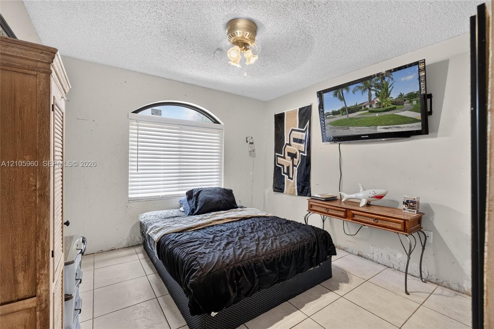 Neutral-toned room featuring light-colored ceramic tile flooring, a prominent arched window with horizontal blinds, and a central ceiling fan with integrated lighting