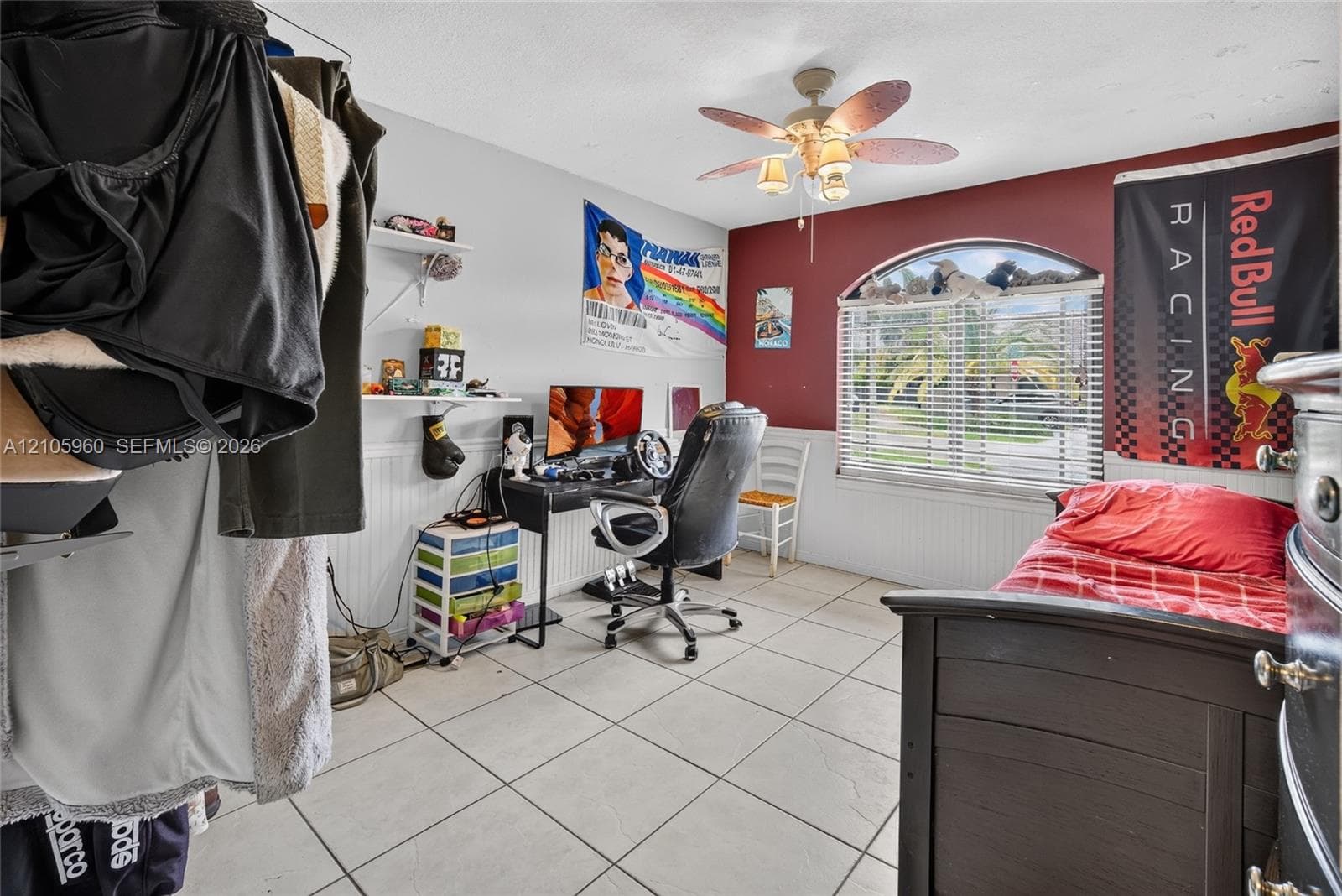 Room featuring large-format tile flooring, arched window with horizontal blinds, beadboard wainscoting, and a multi-blade ceiling fan with integrated lighting