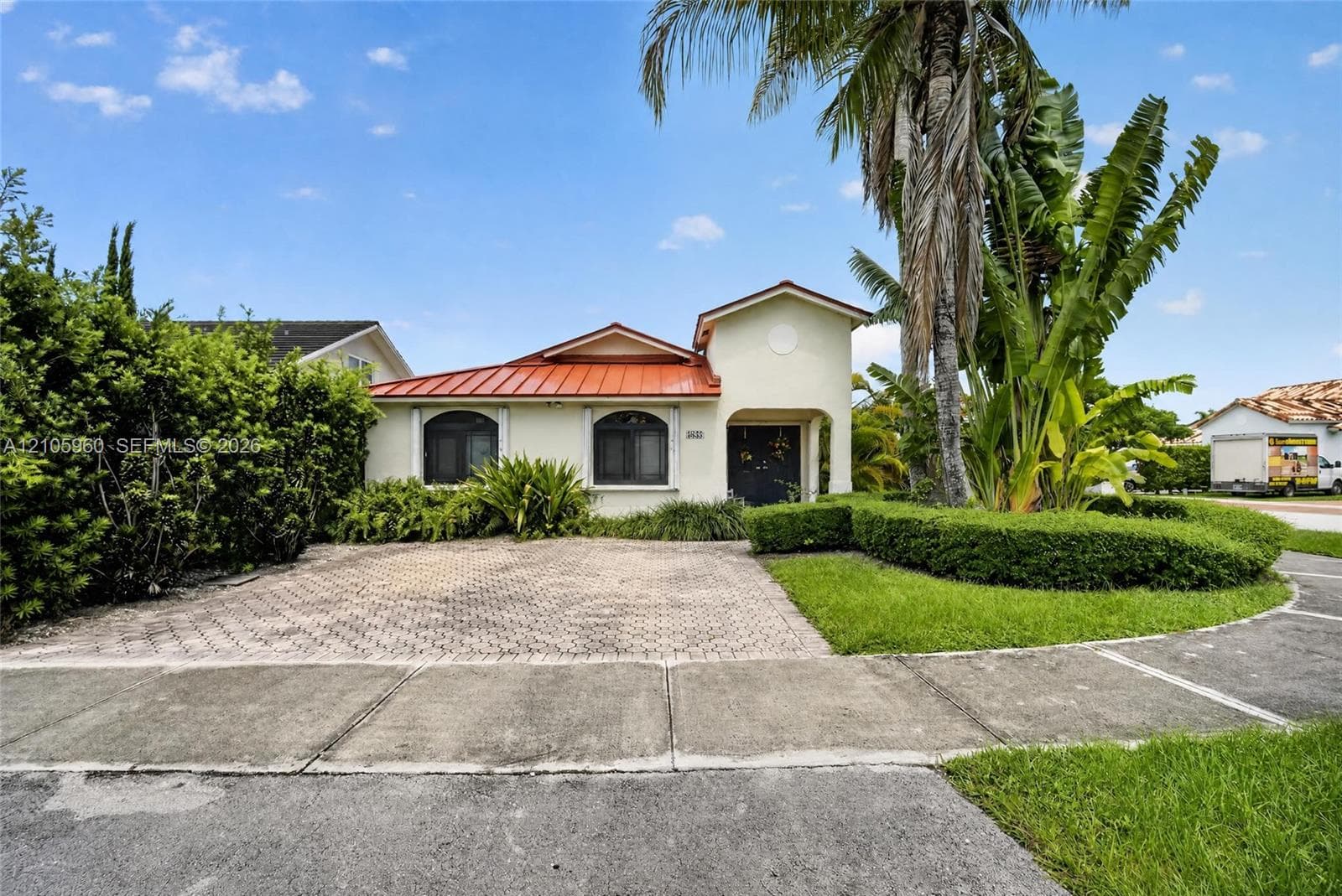 Stucco exterior with a metal roof, arched window casings, and a paved driveway