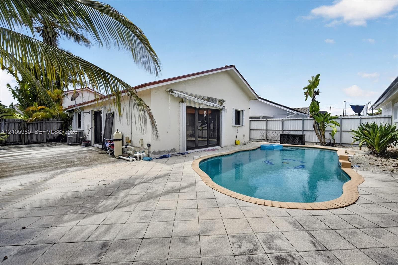 Exterior space featuring a swimming pool, concrete paver patio, retractable awning, and privacy fencing