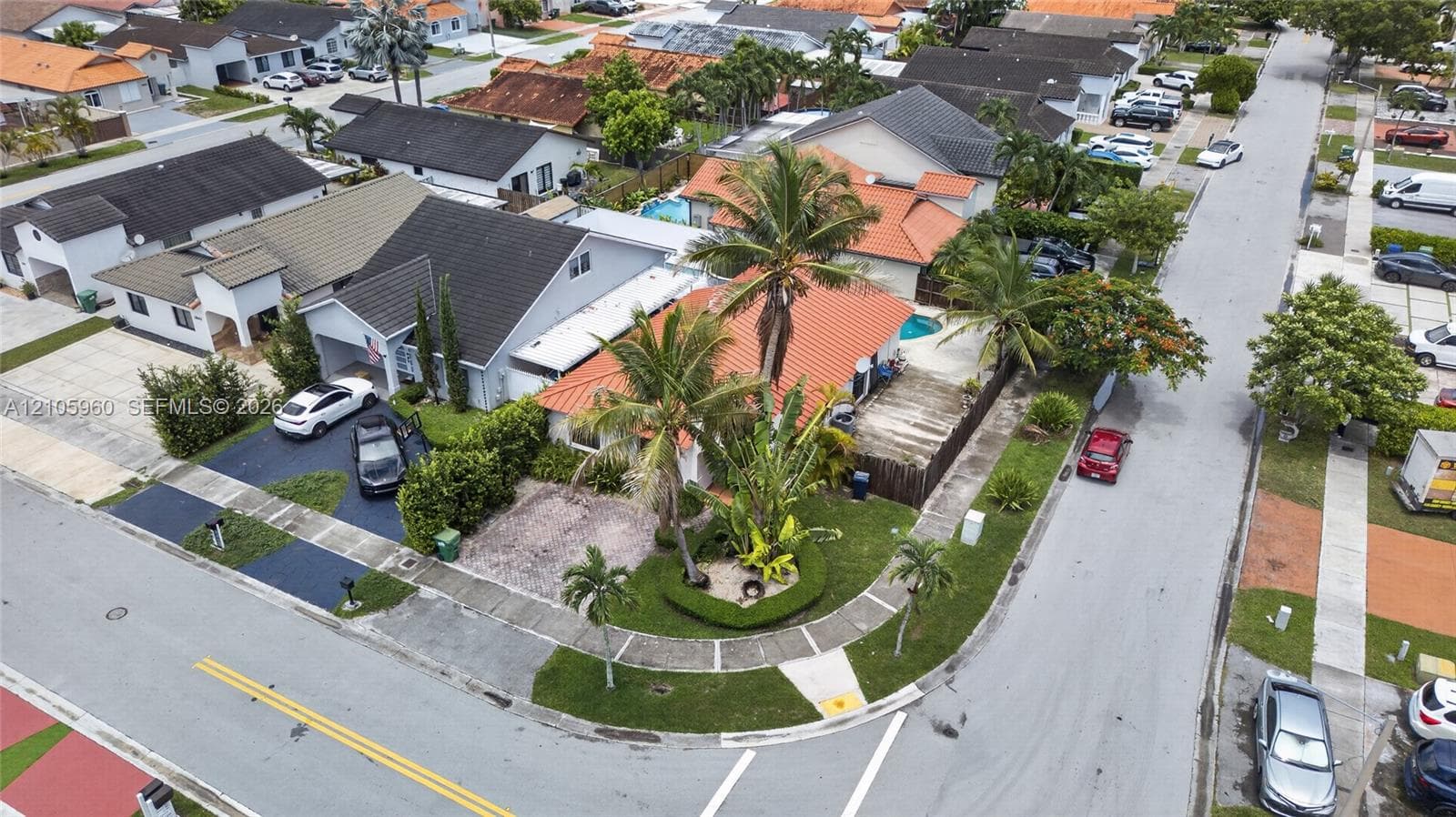 Corner lot residence featuring a barrel tile roof, expansive palm-lined landscaping, and an enclosed backyard with a private swimming pool