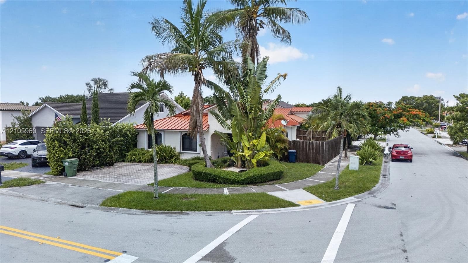 Corner lot exterior featuring a metal roof, paver driveway, manicured landscaping, and mature palm trees