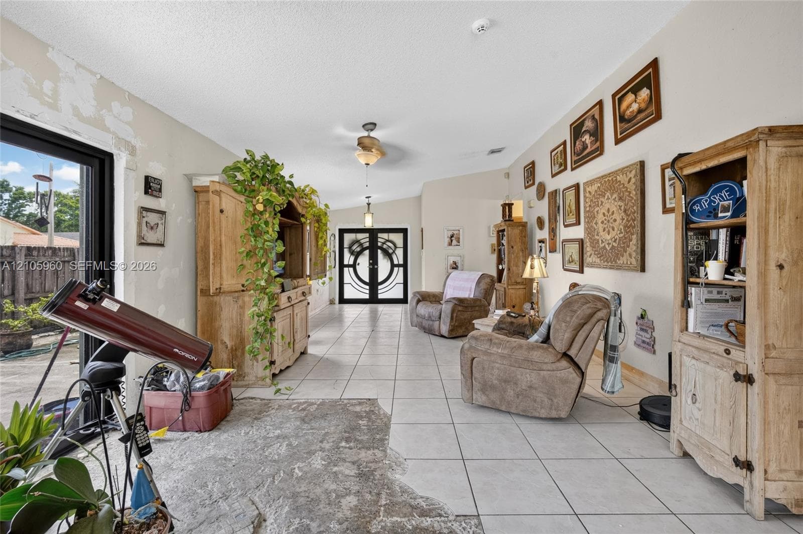 Open-concept living space featuring neutral ceramic tile flooring, dual-entry glass front doors, and a vaulted ceiling with integrated light fixtures