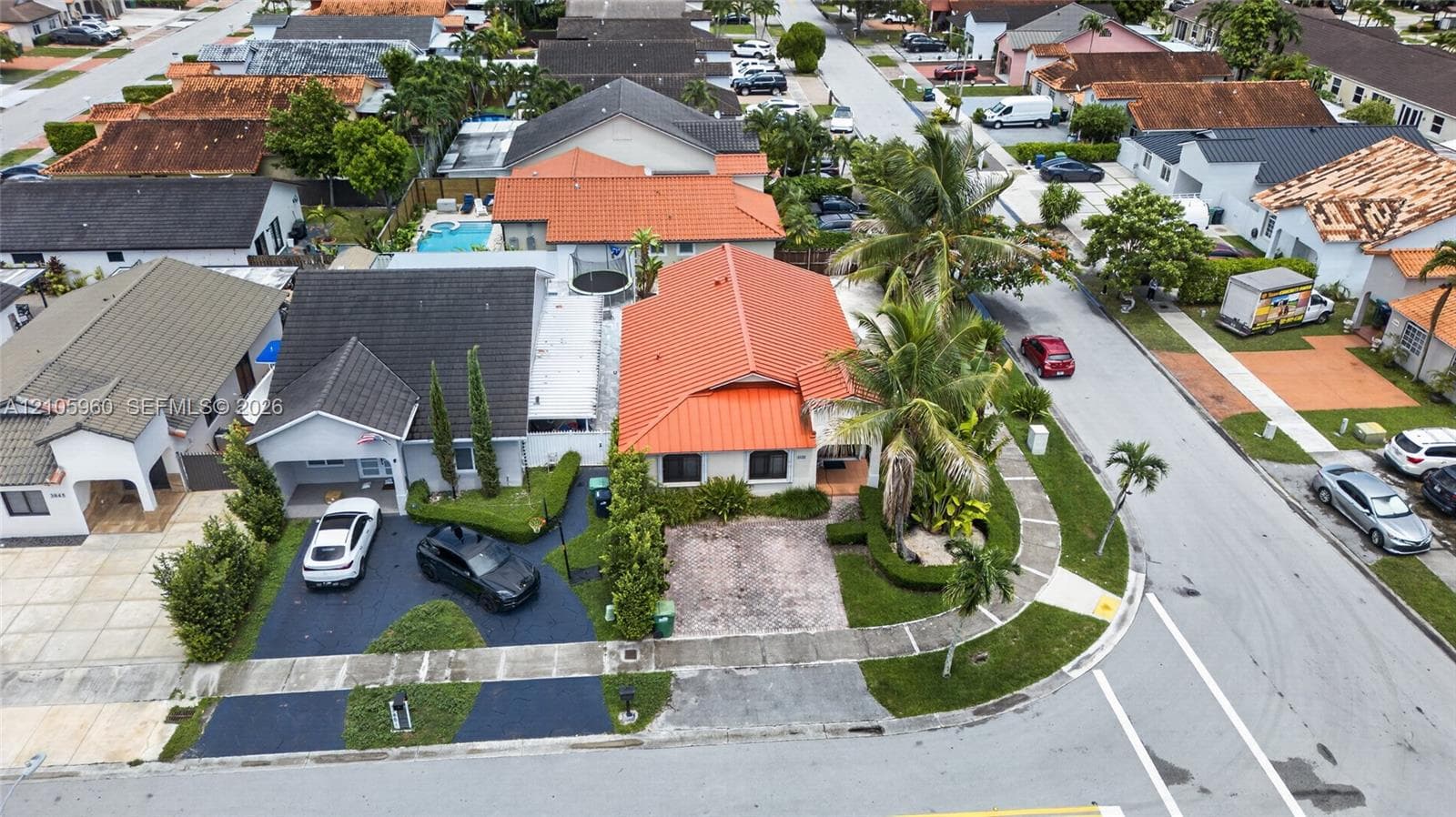 Corner lot residential property featuring a metal tile roof, paved driveway, and manicured landscaping