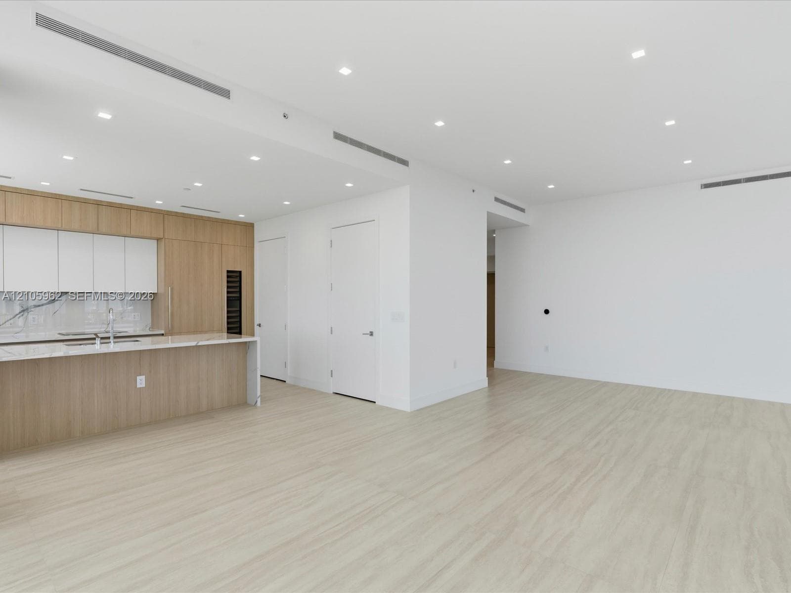 Open-concept area featuring light-toned wood-finish flooring, recessed ceiling lighting, a kitchen island with stone countertop, built-in cabinetry, and integrated refrigeration