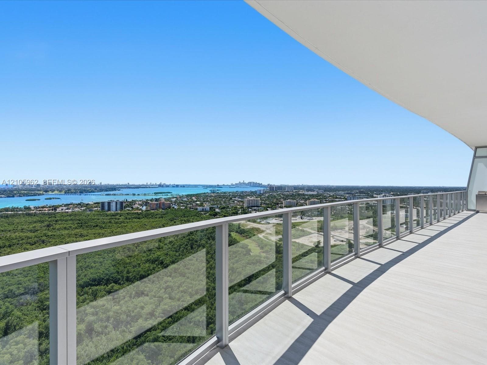 Expansive covered balcony featuring glass panel railings, light-toned decking, and panoramic scenery of the surrounding water and landscape