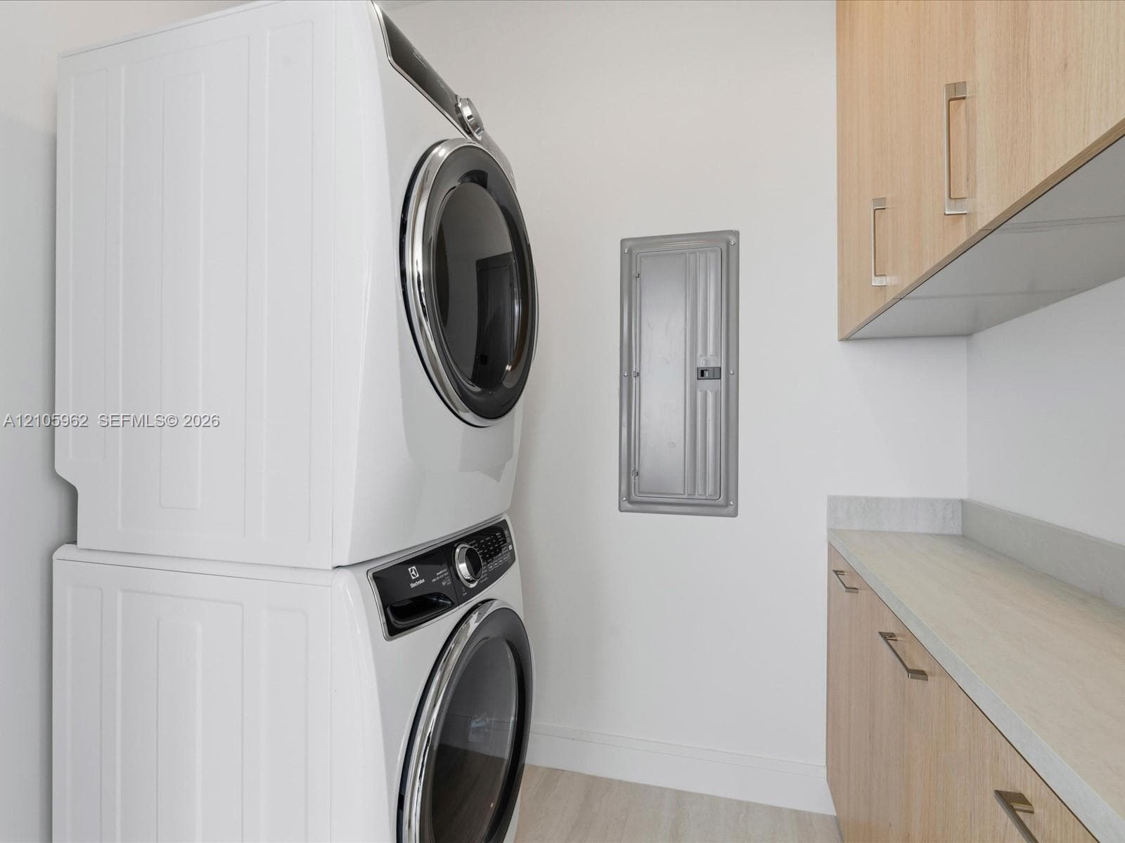 Laundry area featuring stacked appliances, light wood-tone cabinetry, and a stone-surface countertop