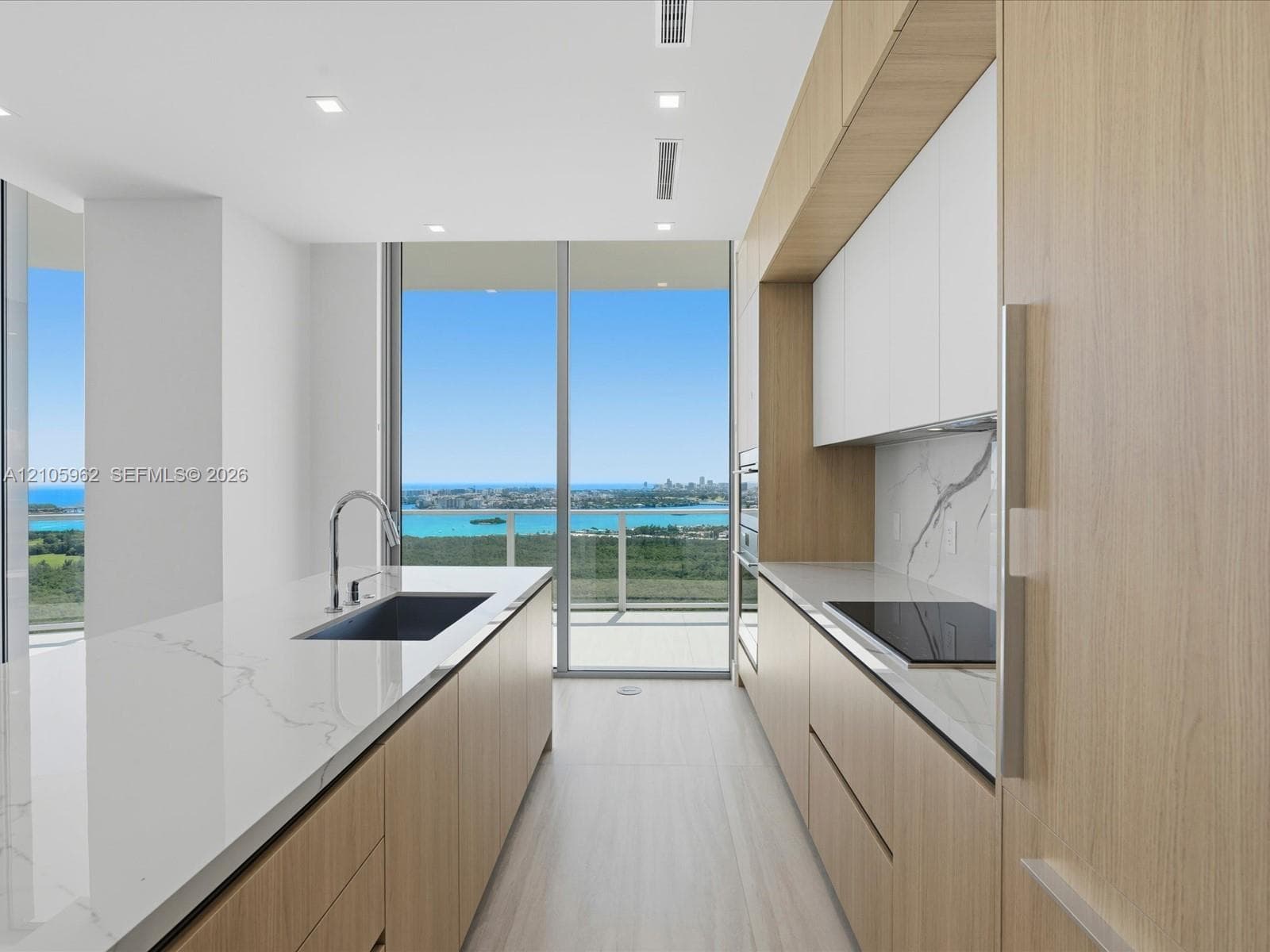 Modern kitchen featuring wood-finish cabinetry, stone-patterned countertops, integrated cooktop, recessed lighting, and floor-to-ceiling sliding glass doors