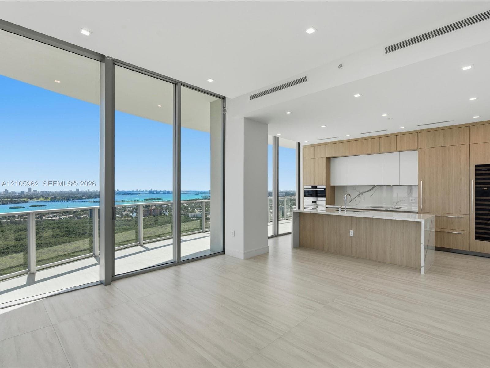 Floor-to-ceiling glass windows, expansive balcony, open-concept kitchen with wood-finish cabinetry, built-in stainless steel appliances, and large-format tile flooring