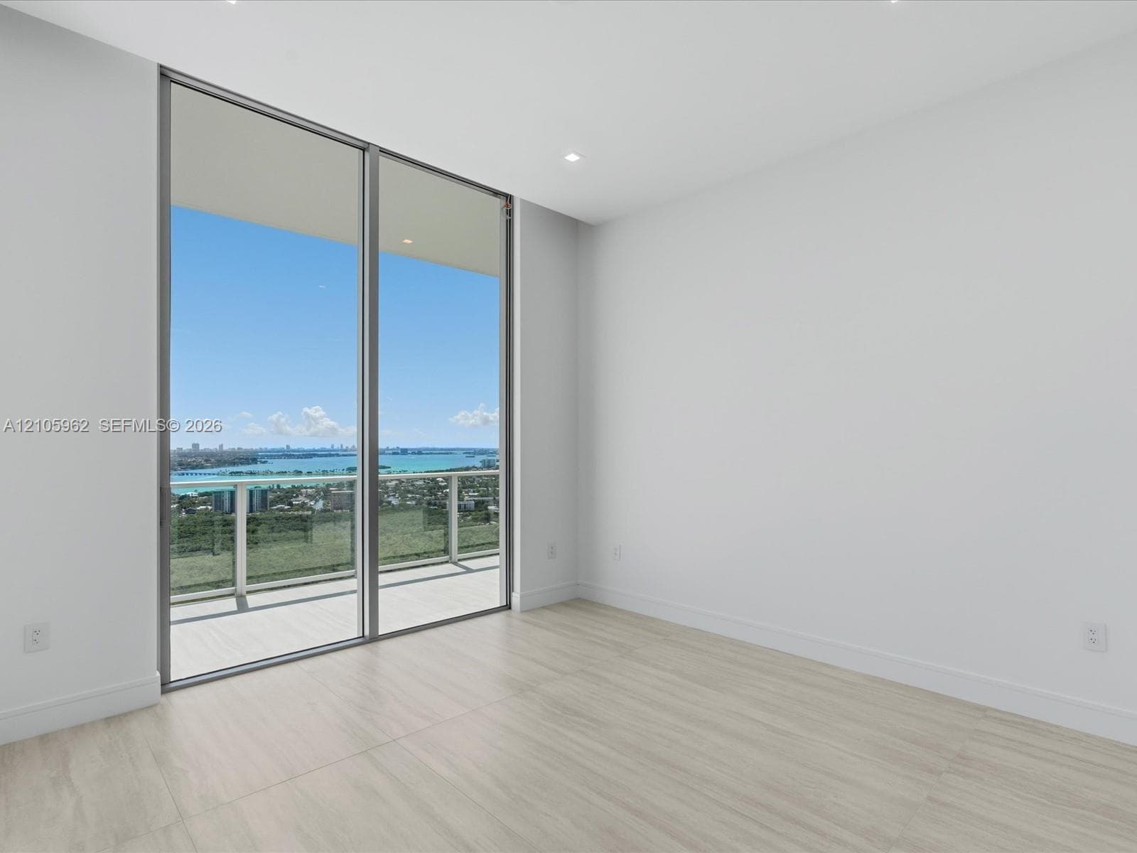 Floor-to-ceiling sliding glass doors, neutral wood-finish flooring, recessed lighting, and a private balcony with metal railing