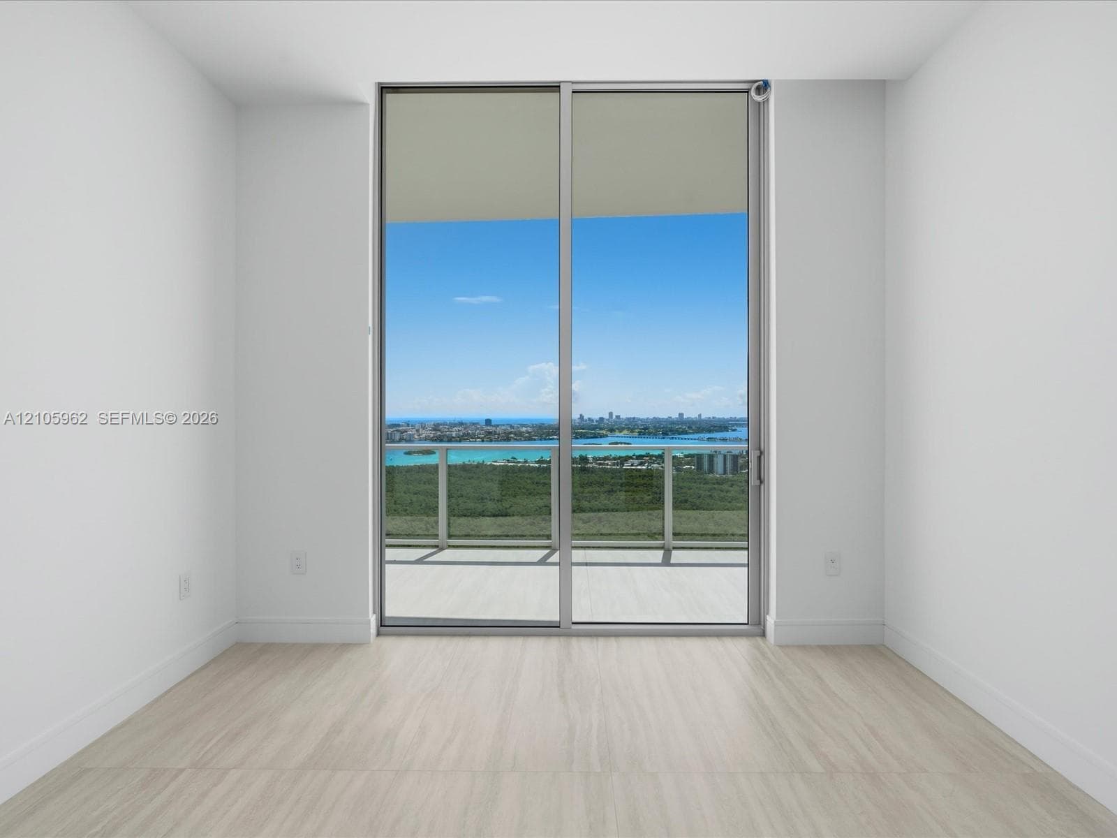 Floor-to-ceiling sliding glass doors, neutral wood-finish flooring, and an attached balcony with metal railing