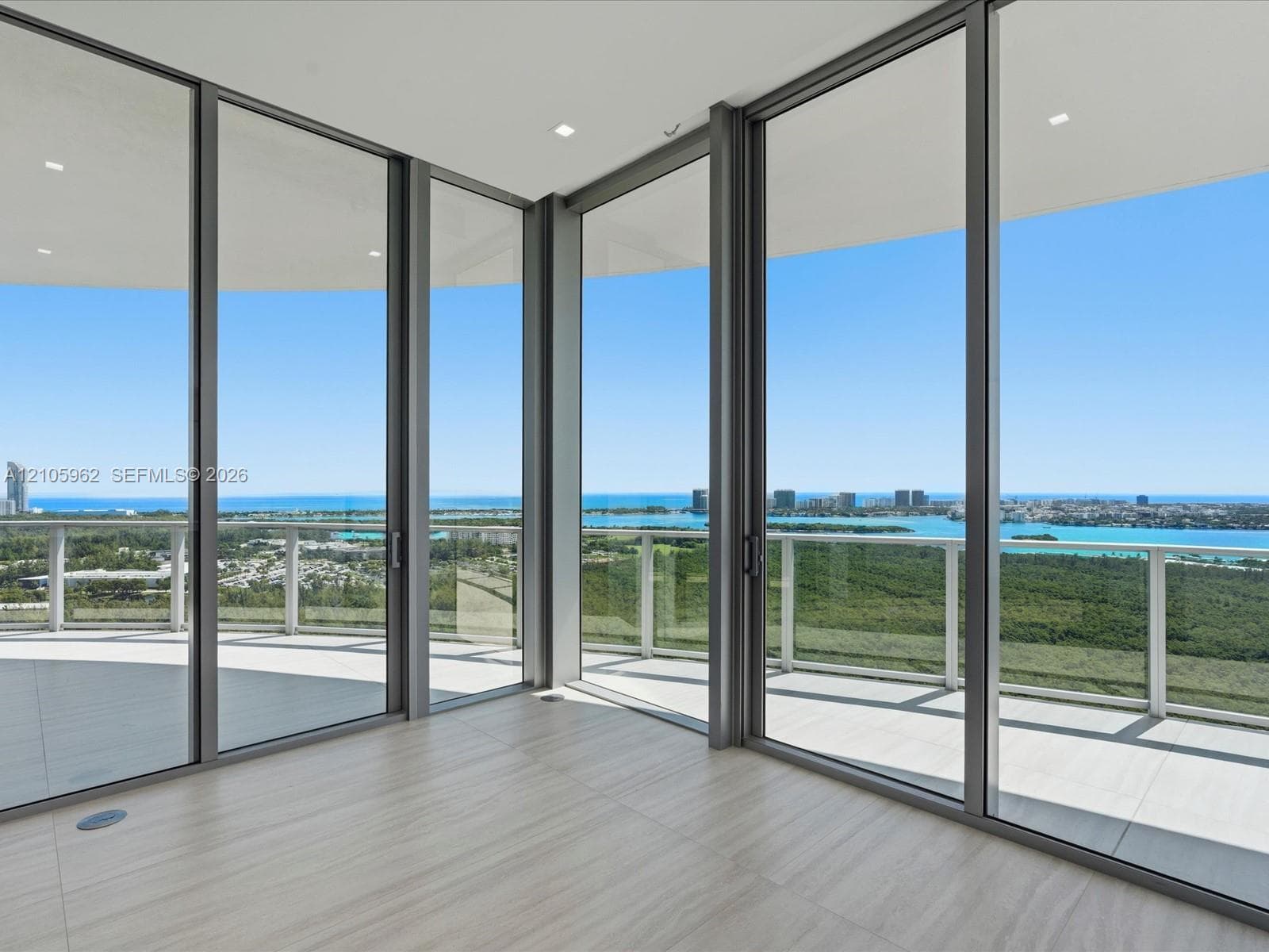 Floor-to-ceiling glass walls with metal framing, expansive private balcony, neutral tile flooring, and recessed ceiling lighting