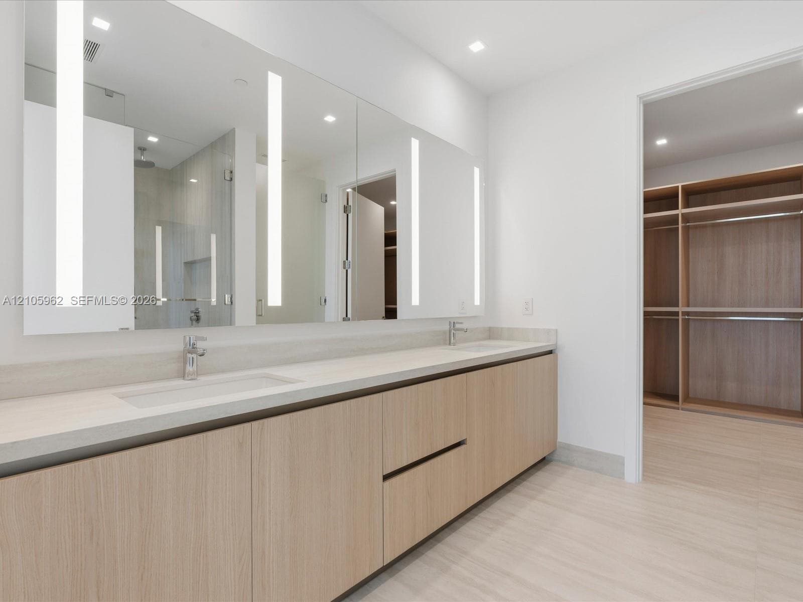 Floating double vanity with integrated sinks, neutral solid-surface countertop, floor-to-ceiling mirror with integrated LED lighting, and wood-finish cabinetry