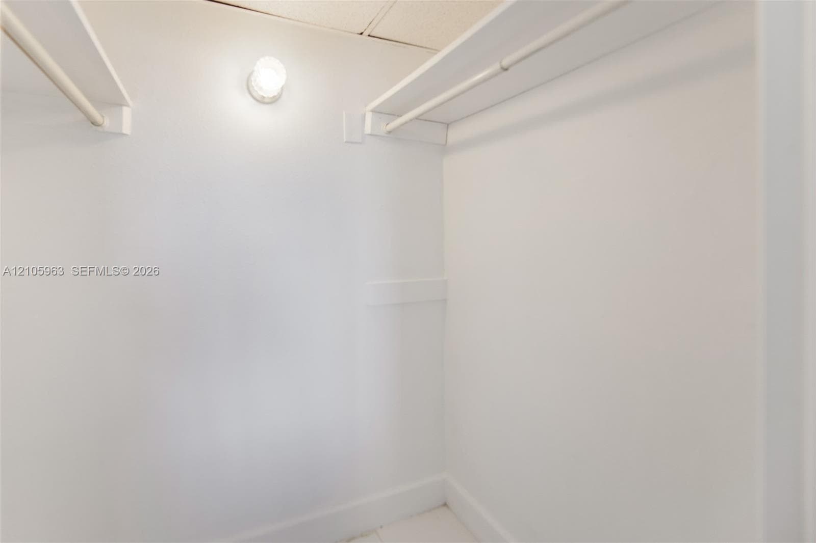 Walk-in closet featuring white walls, dual built-in shelving units, integrated hanging rods, and a ceiling-mounted light fixture