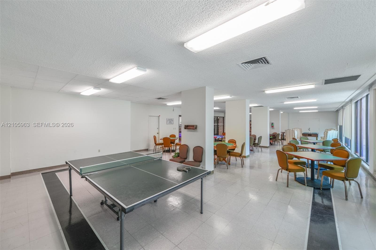 Large open-concept interior featuring light-colored tile flooring with decorative dark accents, structural support pillars, and linear ceiling-mounted lighting