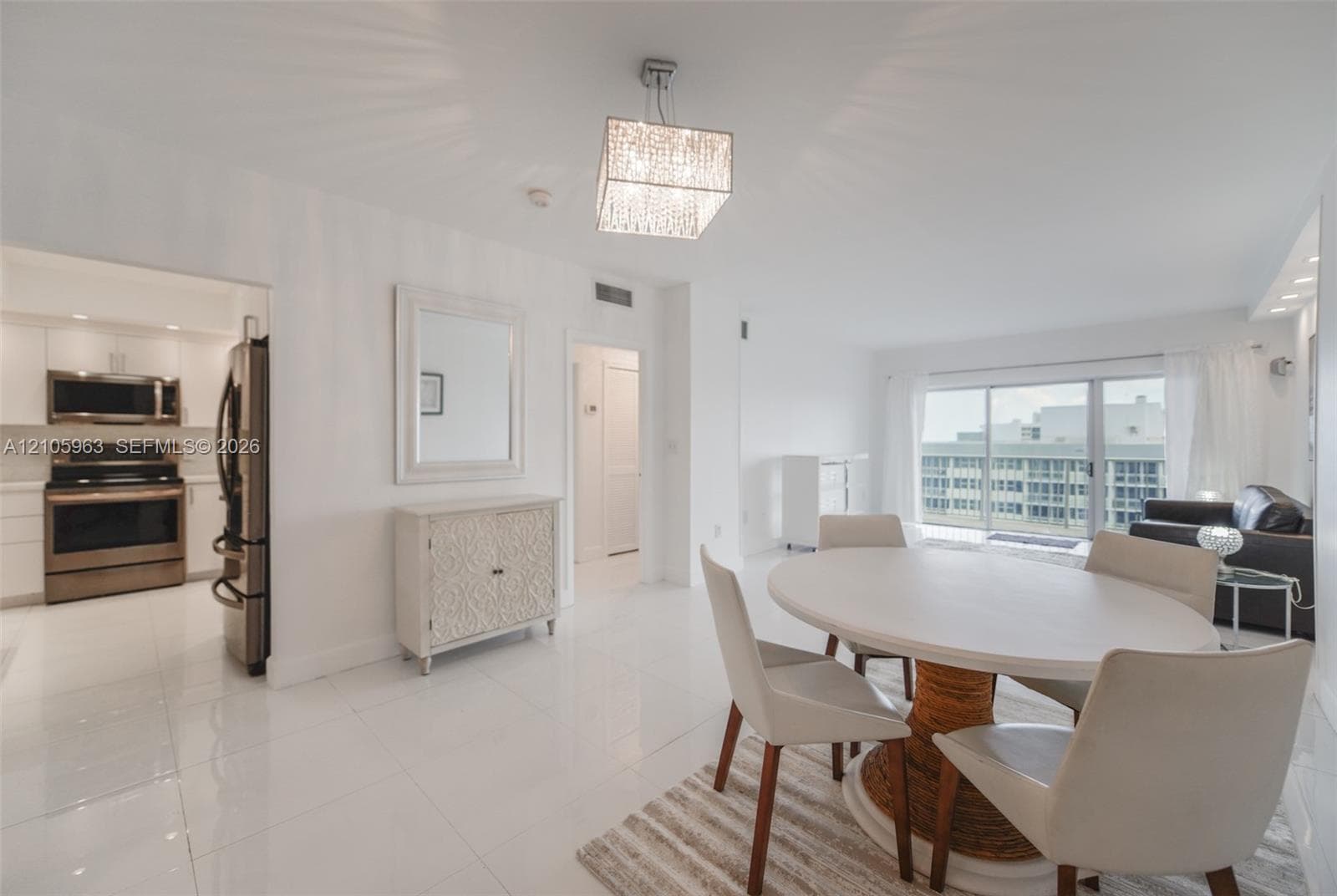 Open-concept living space featuring high-gloss tile flooring, recessed lighting, a modern square crystal chandelier, and large sliding glass doors providing natural light