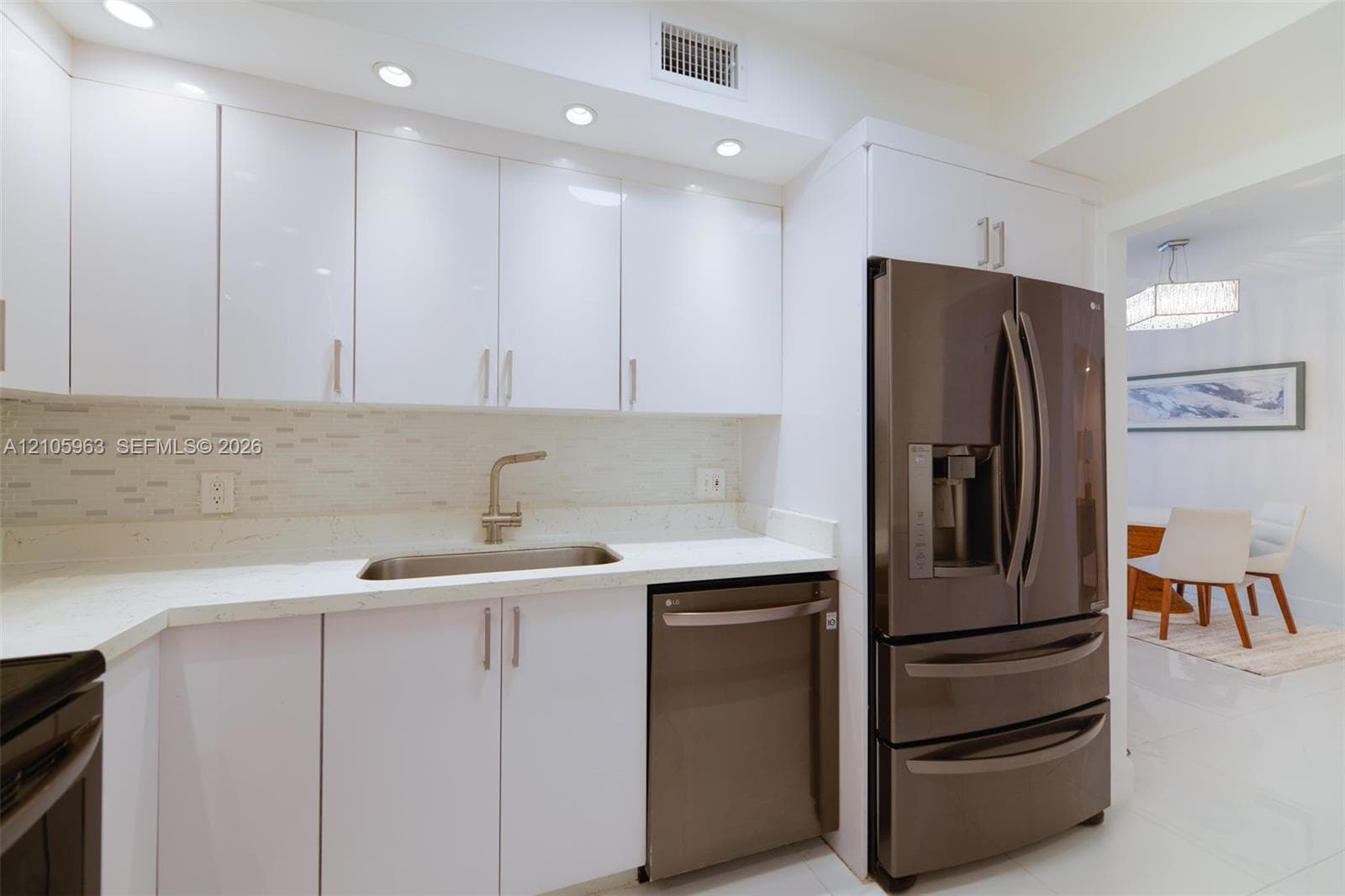 Kitchen featuring high-gloss white cabinetry, light-toned stone-surface countertops, a mosaic tile backsplash, stainless steel appliances, and recessed lighting