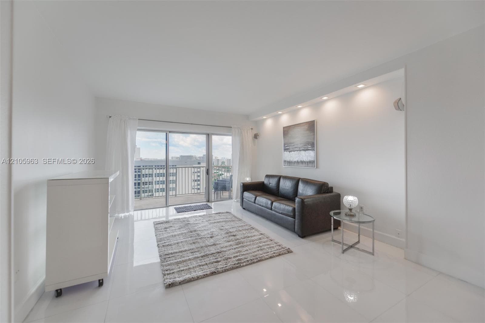 Living area featuring polished tile flooring, recessed ceiling lighting, and a large sliding glass door opening to a balcony
