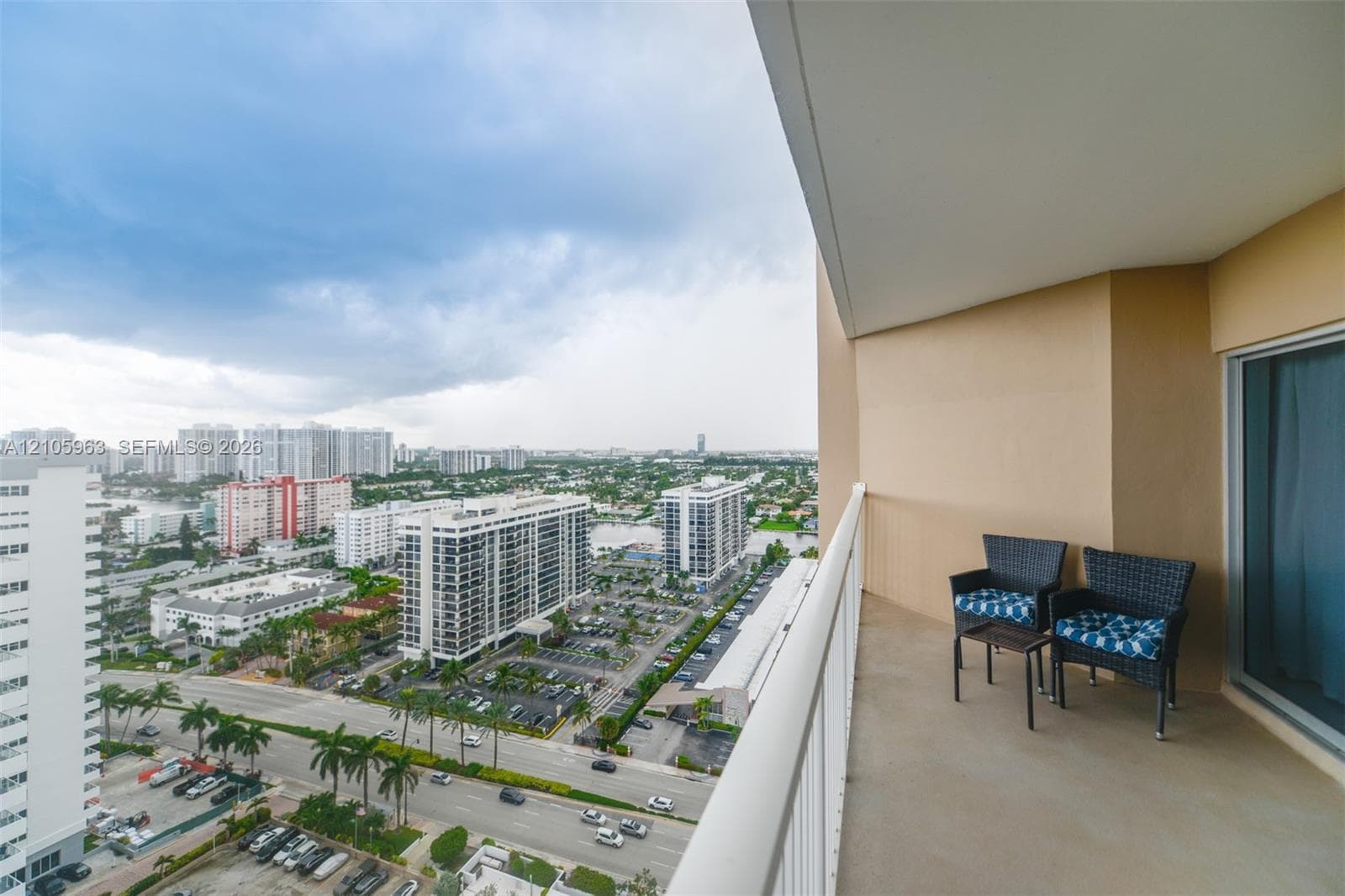 Covered balcony featuring concrete flooring, a protective metal railing, and high-rise urban surroundings
