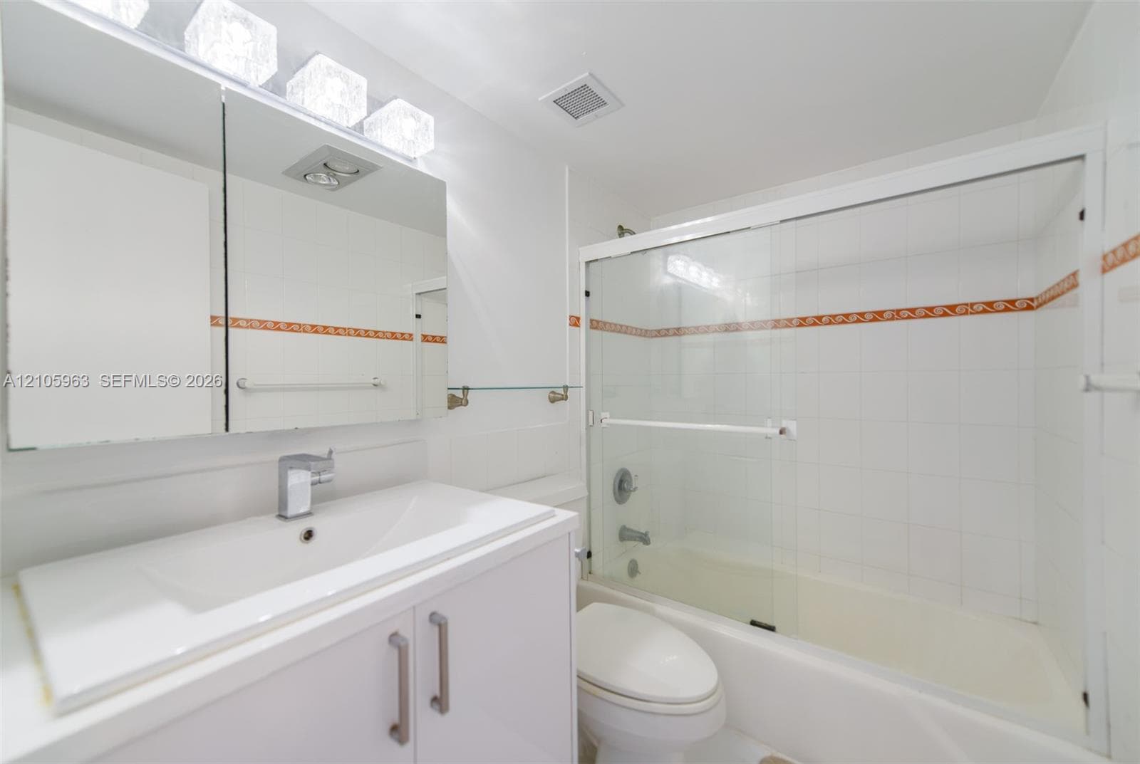 Bathroom featuring a vanity with an integrated sink, tri-light fixture, medicine cabinet, and a tub-shower combination enclosed by glass sliding doors
